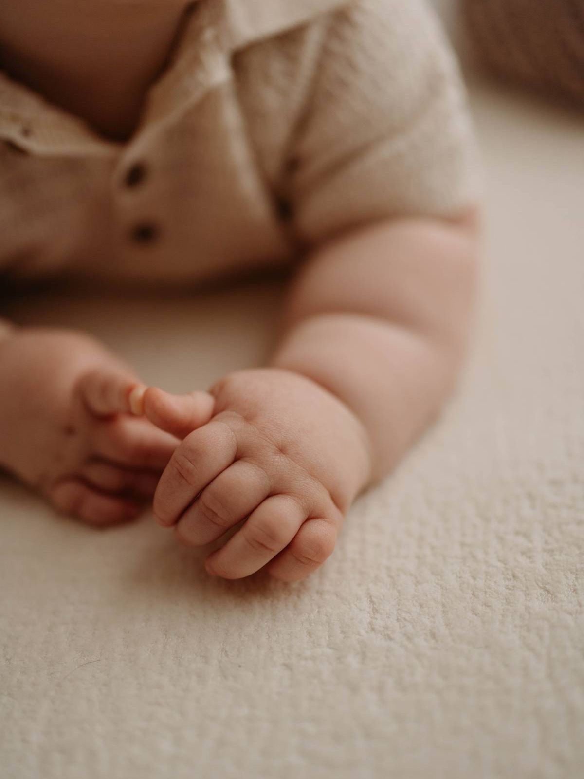 Close-up of chubby newborn baby hands resting on white surface in beige romper. Lafayette indiana tippecanoe county west lafayette