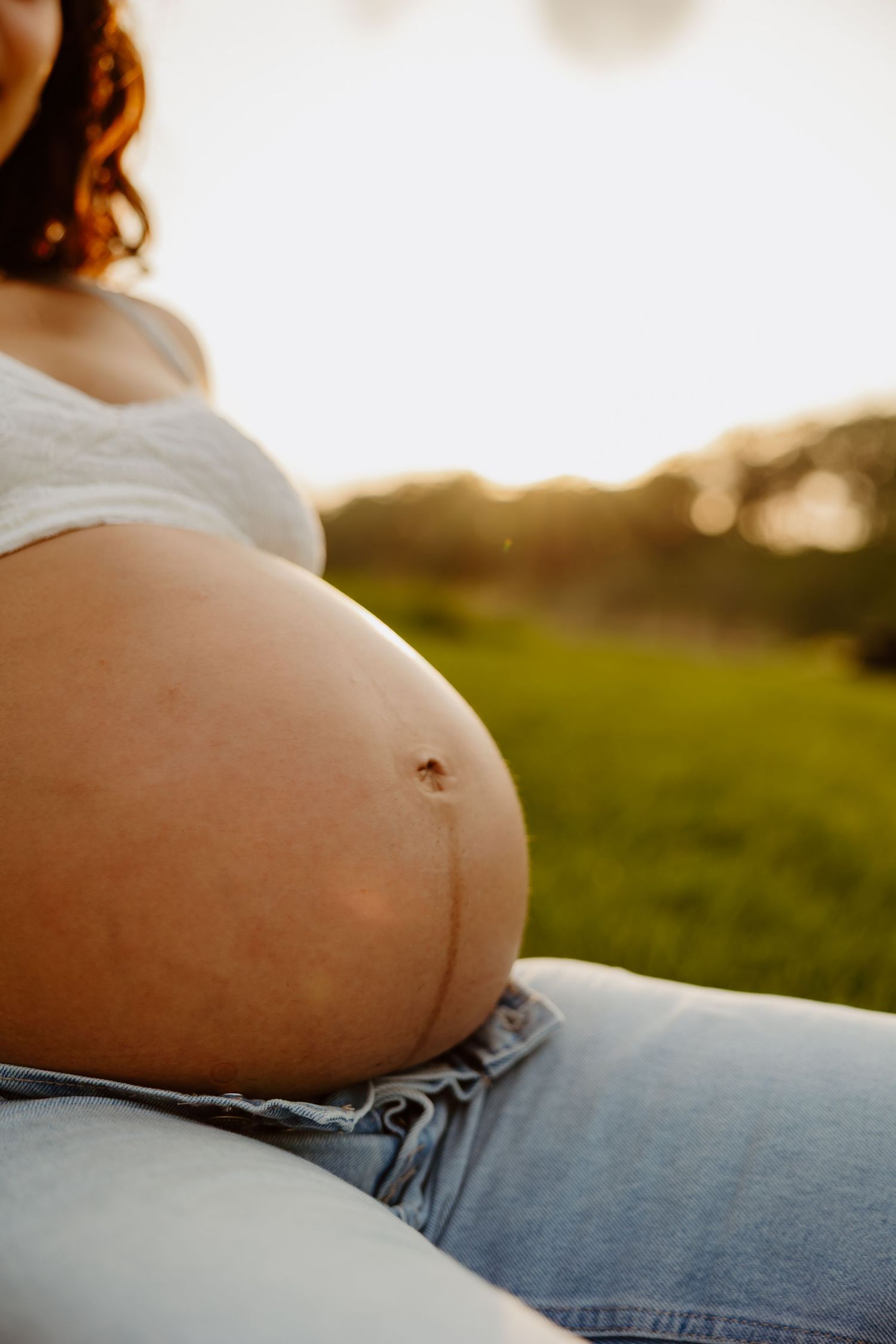 Close-up of pregnant woman's bare belly in jeans outdoors at golden sunset hour. in Lafayette indiana tippecanoe county west lafayette