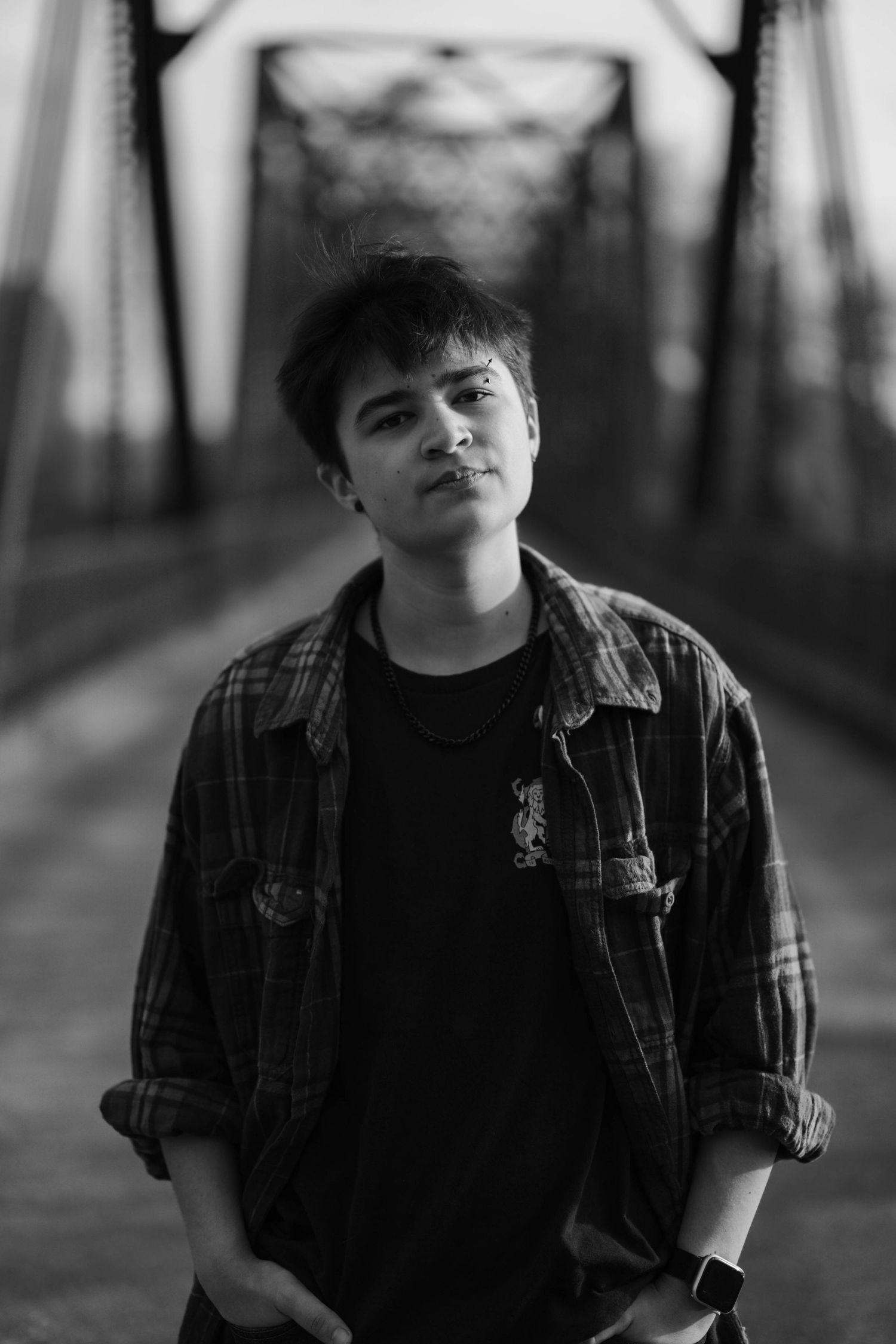 Black and white portrait of a young man in a plaid shirt standing on a steel bridge. High school senior photos in west Lafayette indiana