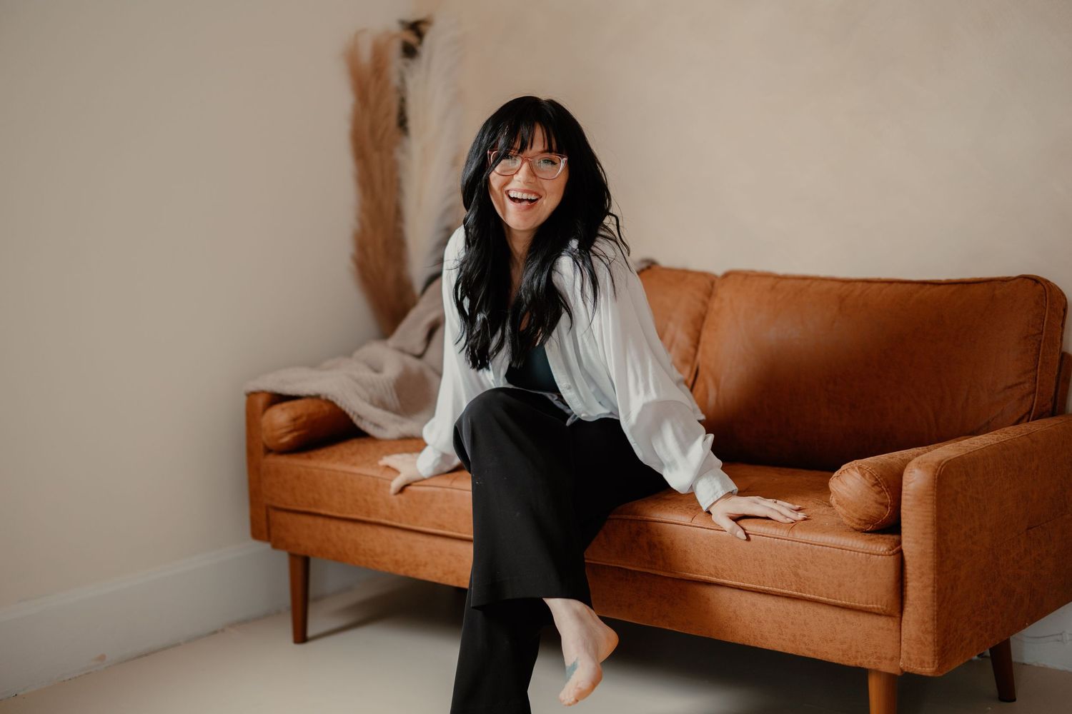 Smiling woman with dark hair laughing while sitting on a brown leather couch. Lafayette indiana tippecanoe county west lafayette
