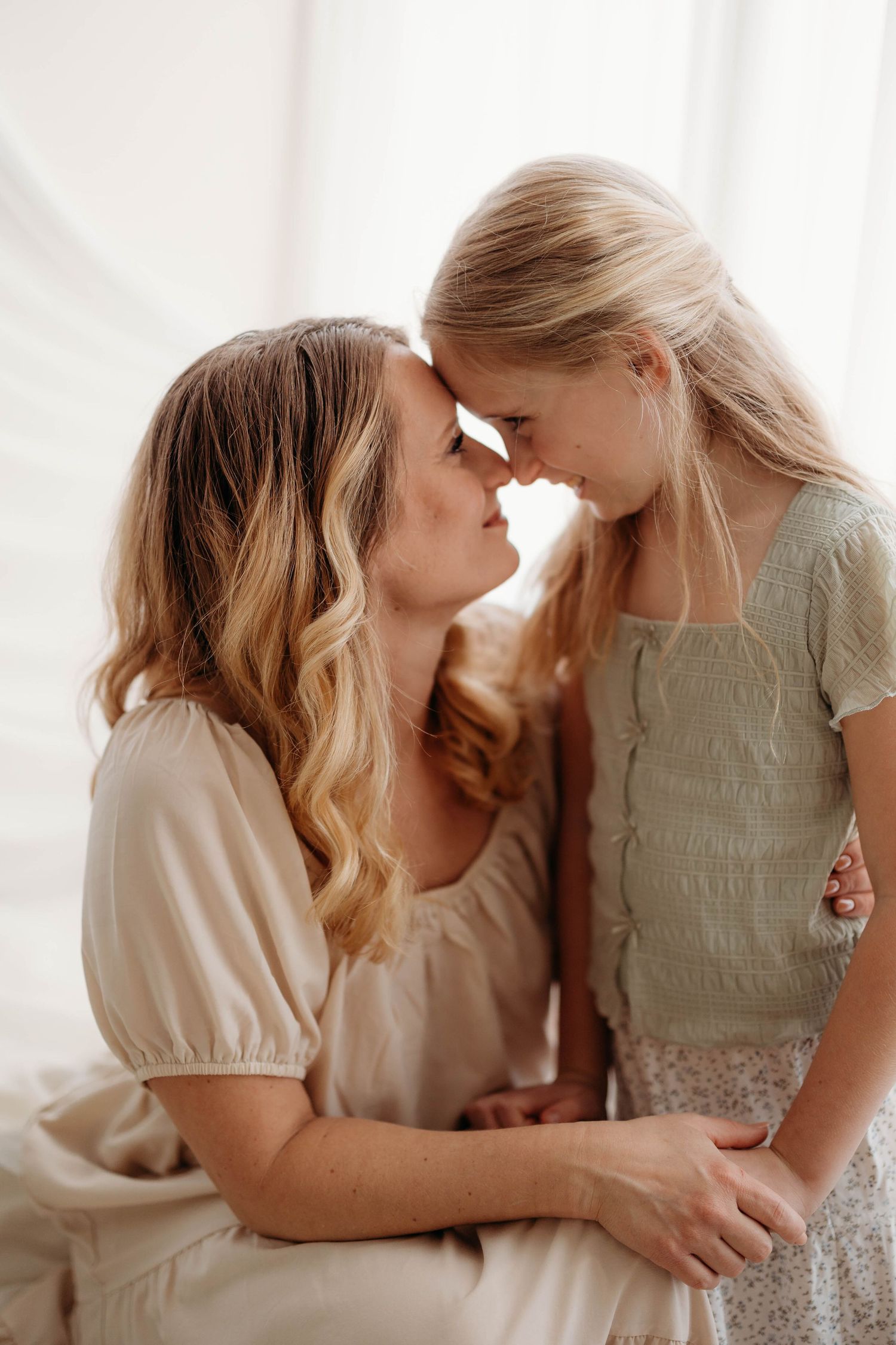 Mother and daughter touching foreheads in tender moment wearing neutral tones in bright studio. in west Lafayette indiana Tippecanoe county