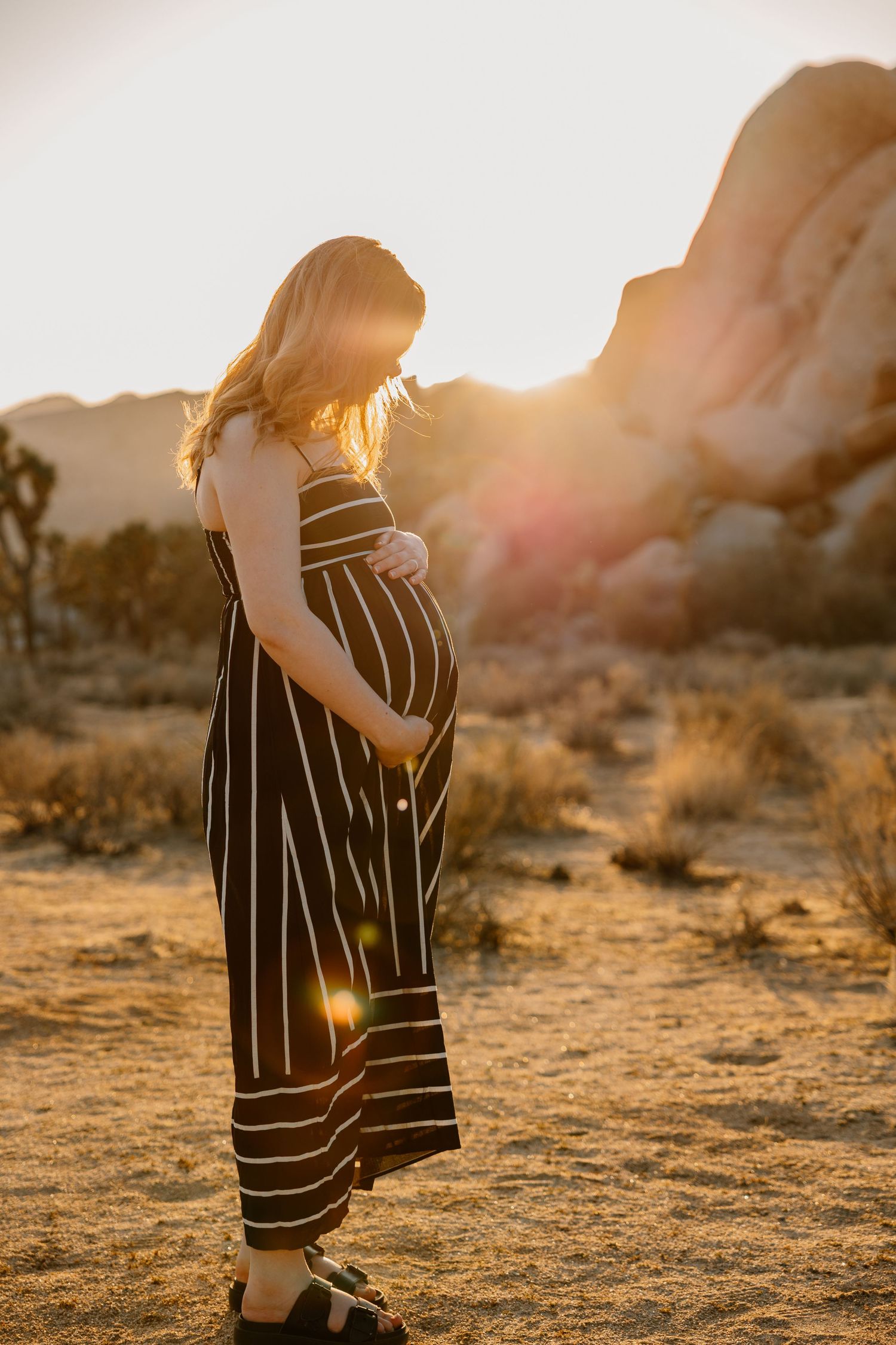 Pregnant woman in black striped dress holding belly with dramatic desert sunset backdrop. Lafayette indiana tippecanoe county maternity