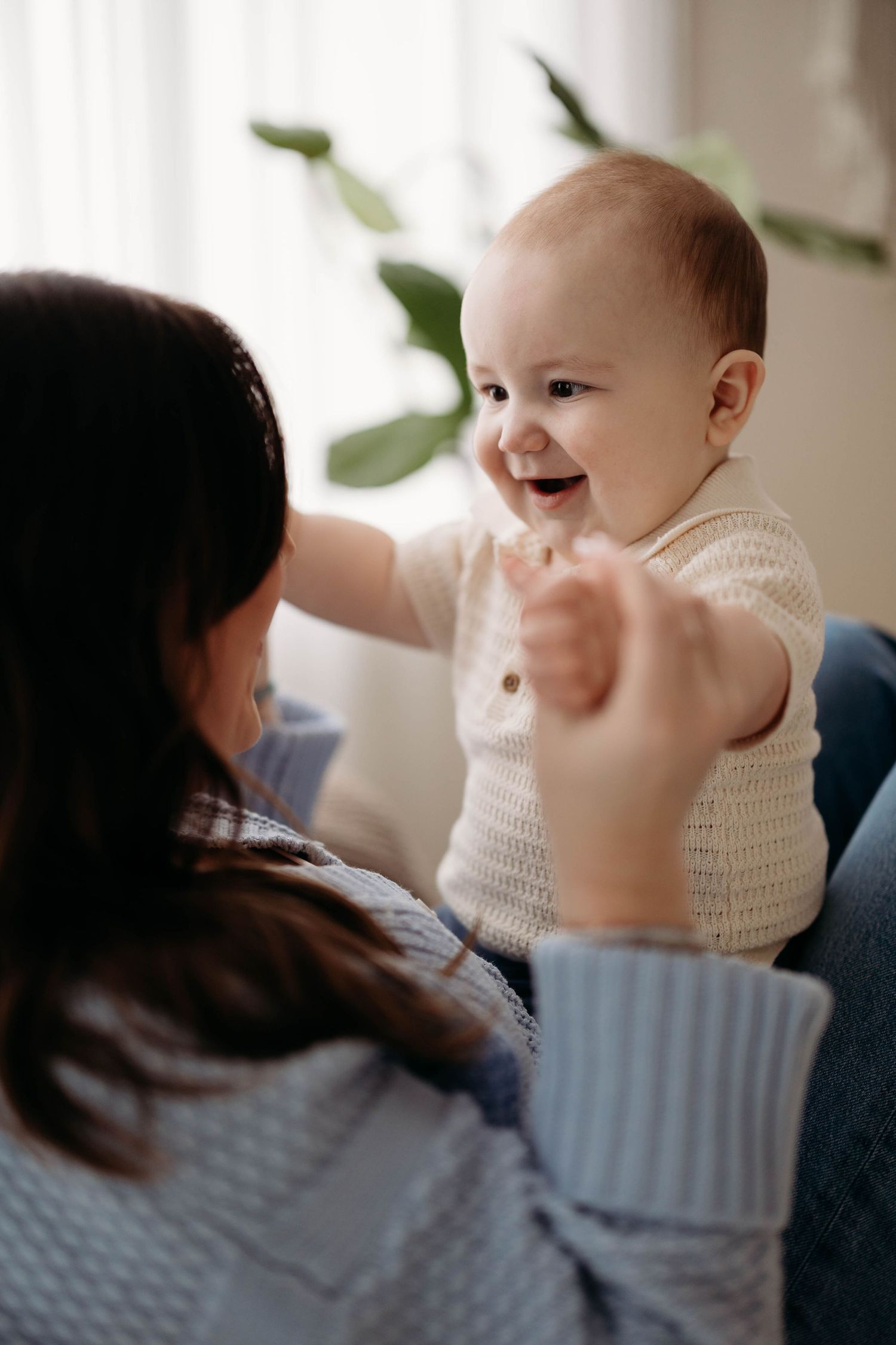 A happy baby laughs and reaches out while being held by their dark-haired mother on a sofa. Lafayette indiana tippecanoe county west lafayet