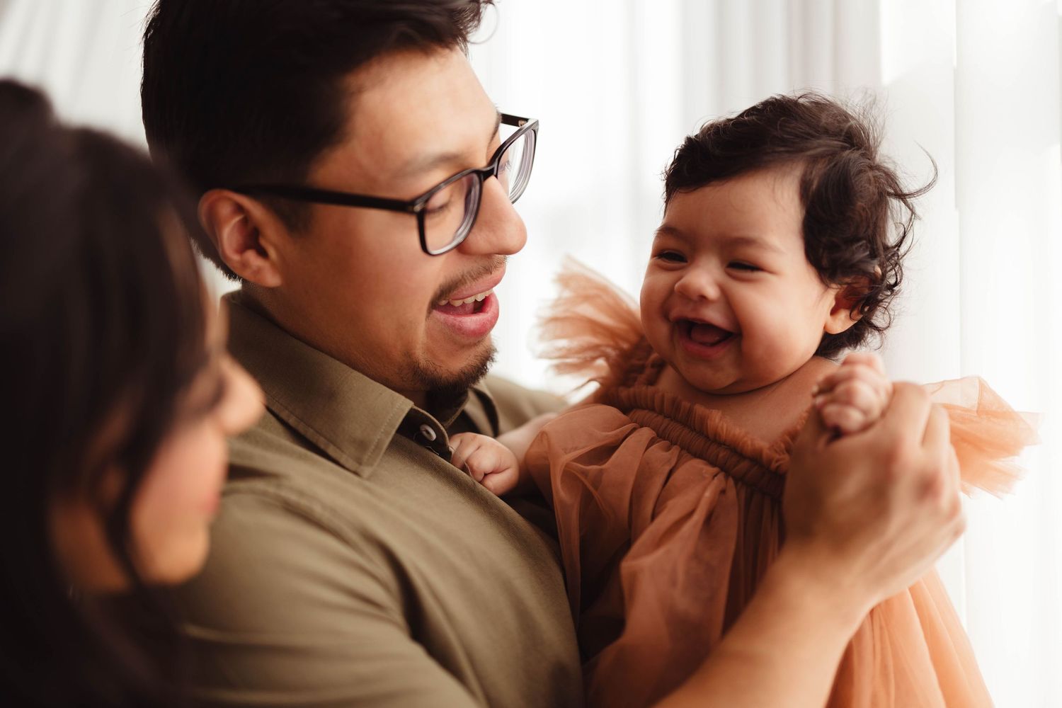 Delighted baby girl in orange tulle dress laughing with father in glasses in bright indoor setting. Lafayette indiana tippecanoe county