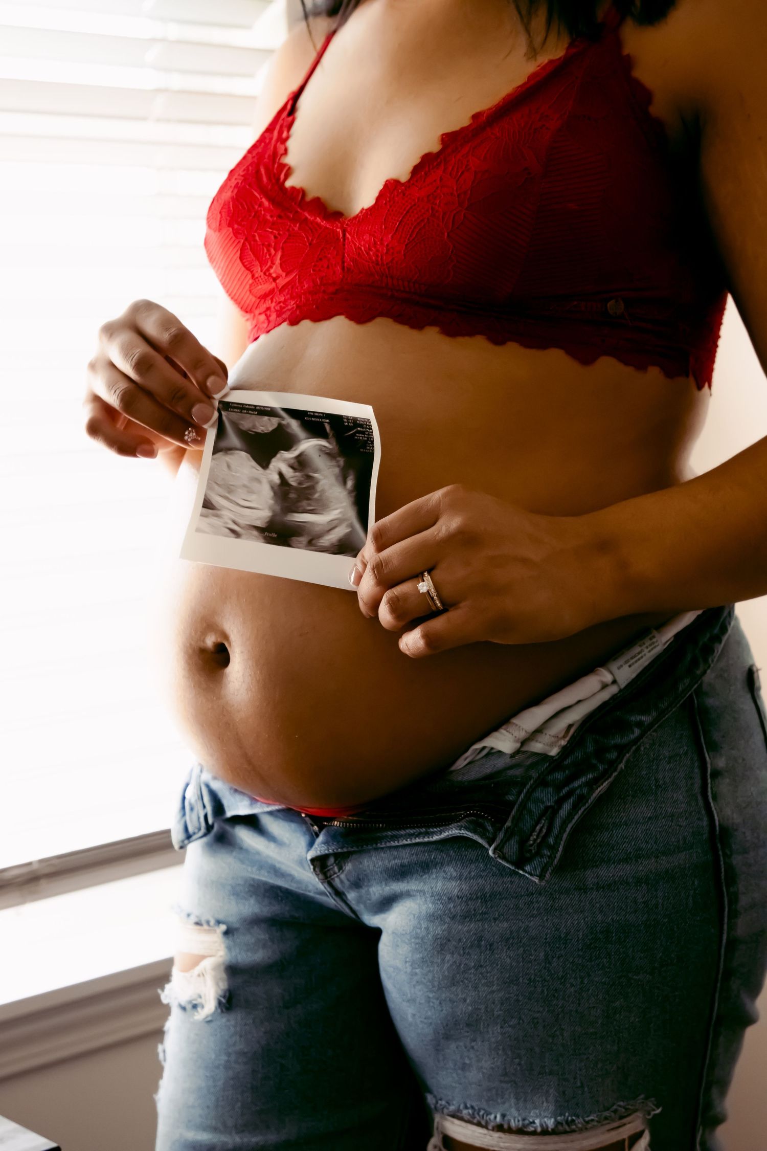 Pregnant woman in red lace bralette holding ultrasound photo near baby bump by window. maternity west Lafayette indiana
