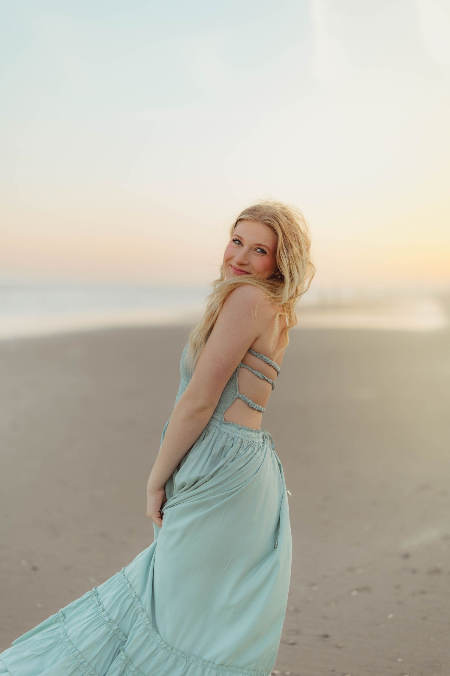 Blonde girl in a mint green backless maxi dress posing on a sandy beach at sunset. High school senior photos in west Lafayette indiana