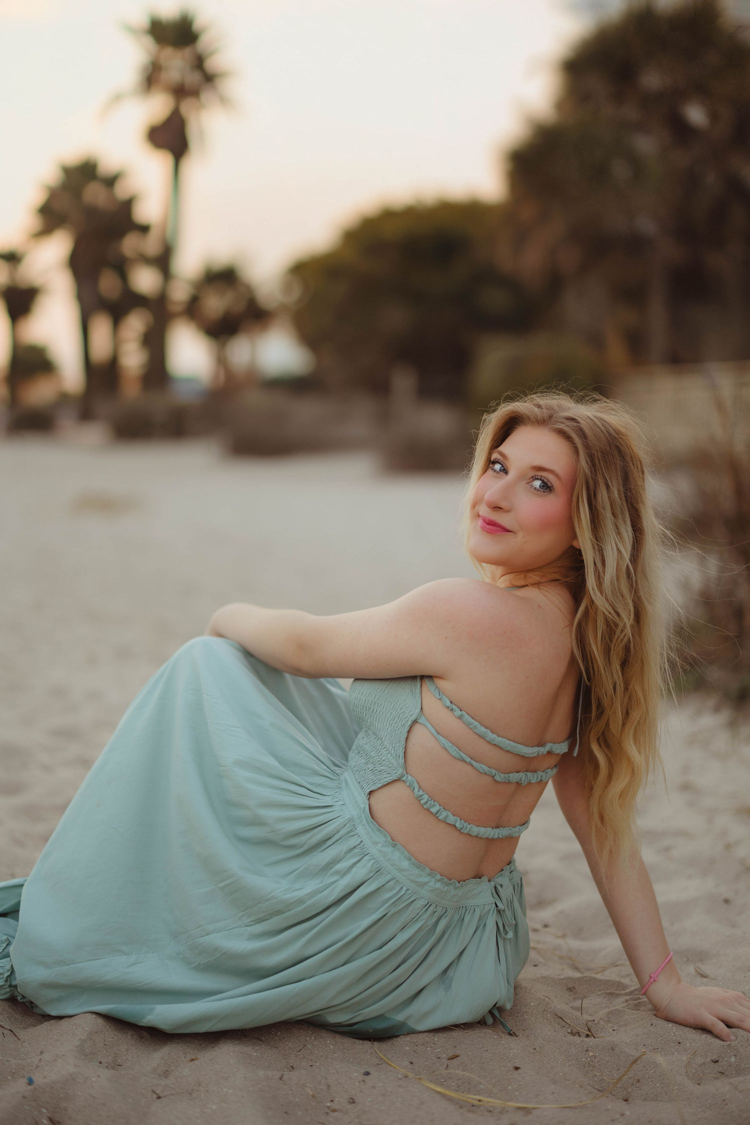 A blonde woman in a backless mint dress sits on sandy beach with palm trees at dusk. Lafayette indiana tippecanoe county west lafayette