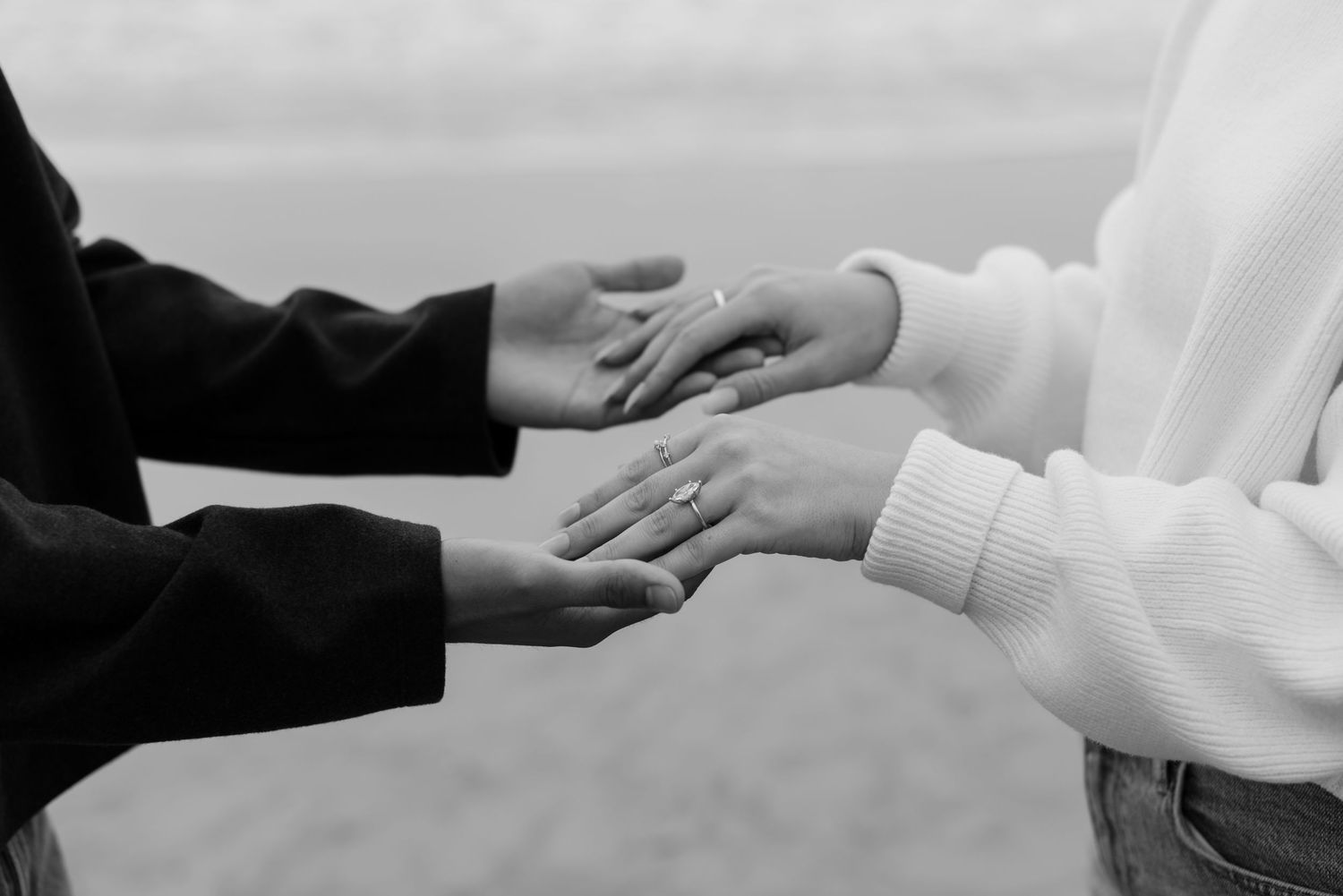 Black and white photo of two people holding hands gently, wearing casual clothing, in an outdoor setting.