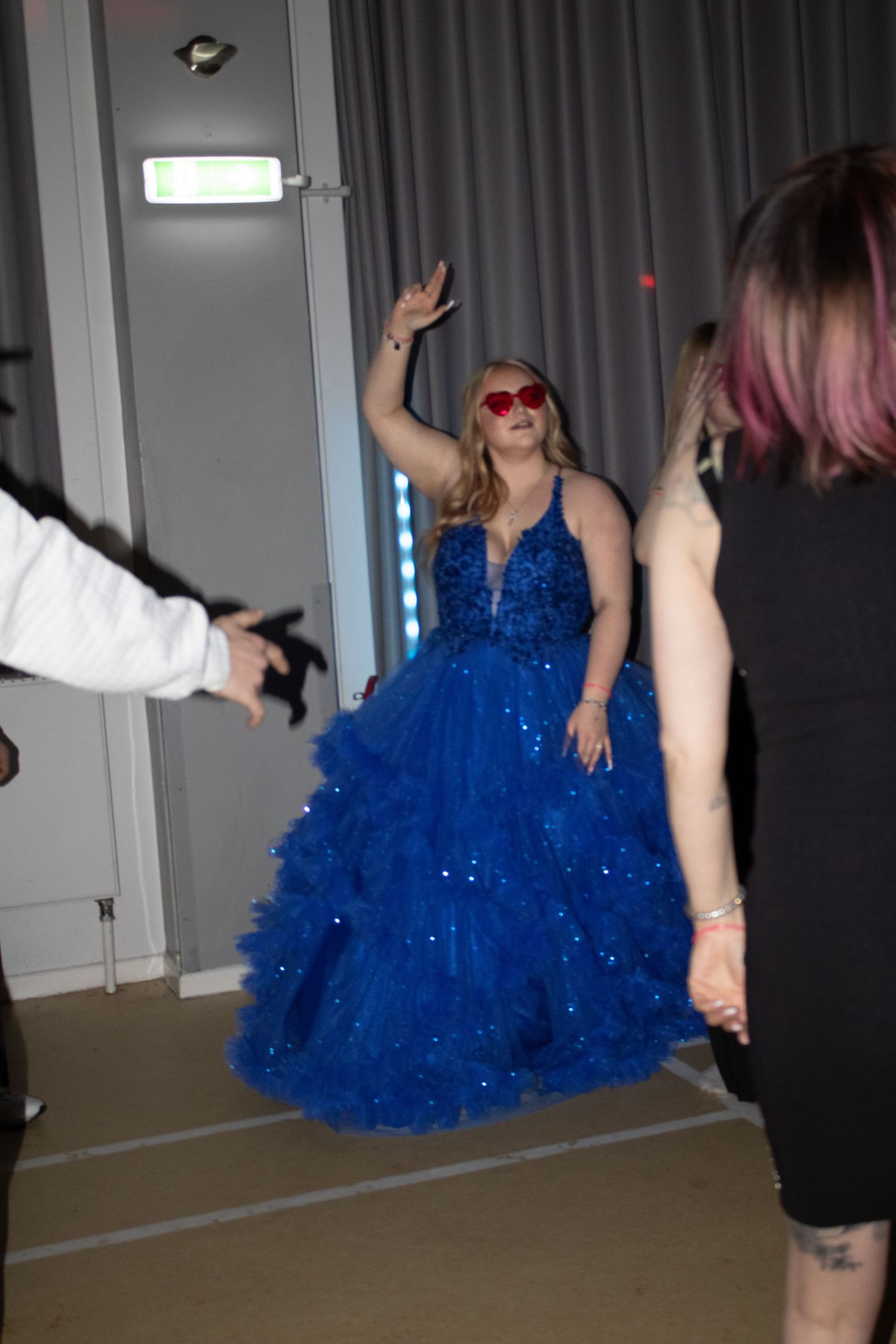 Woman in a royal blue sparkly ball gown with red sunglasses dancing at a formal event.