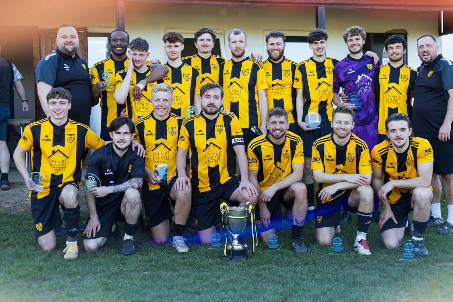 Football team in black and yellow striped jerseys posing with a trophy after a match.