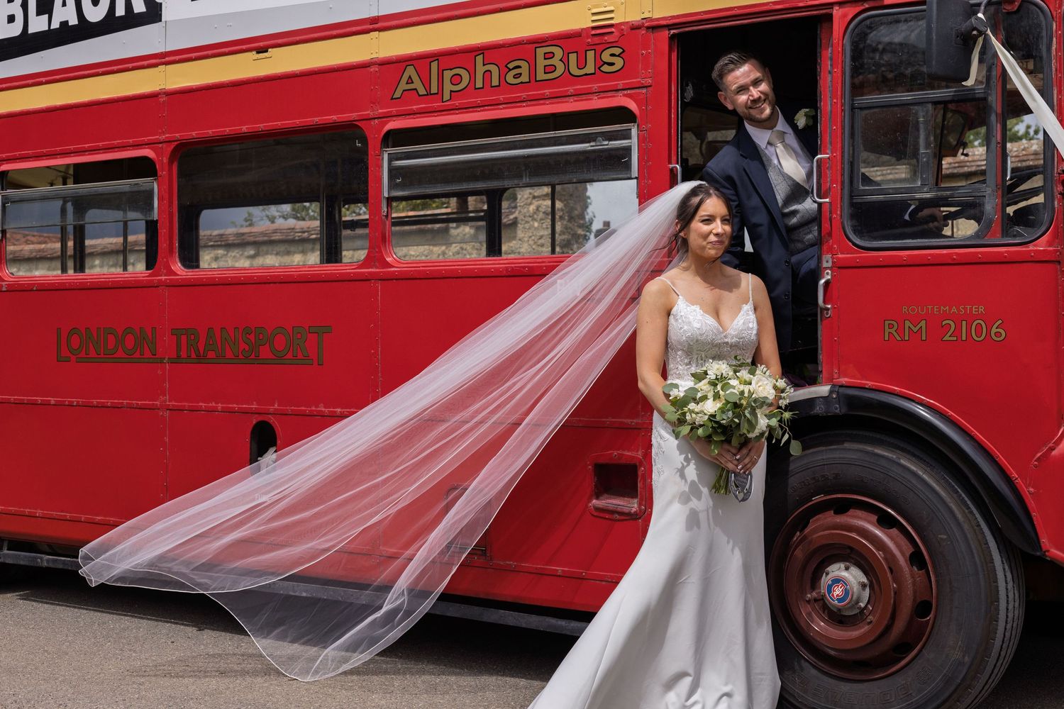 Bride and groom posing beside a vintage red London Transport AlphaBus double-decker bus on their wedding day.