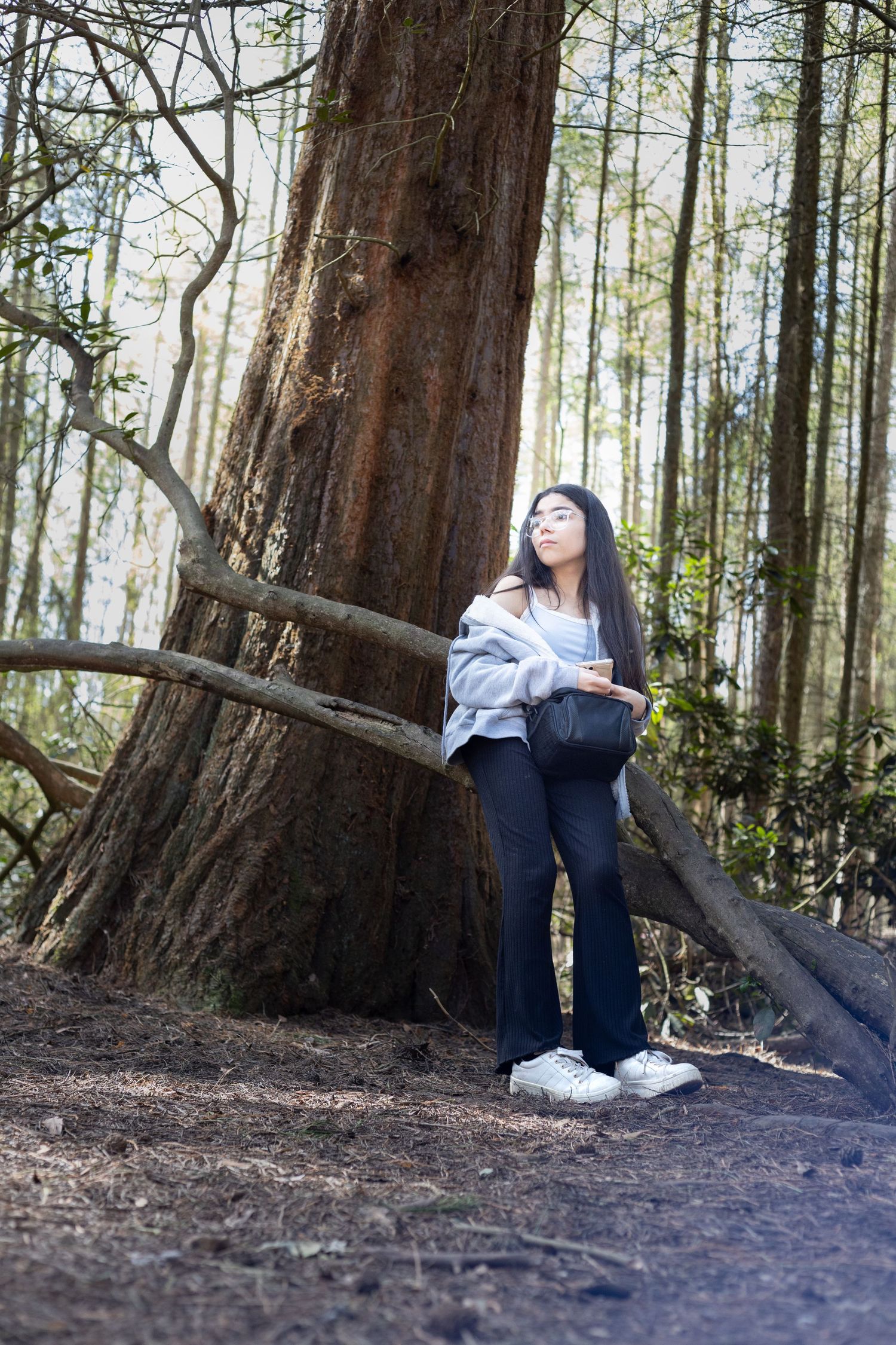 Young woman leaning against a large tree trunk in a serene forest setting.