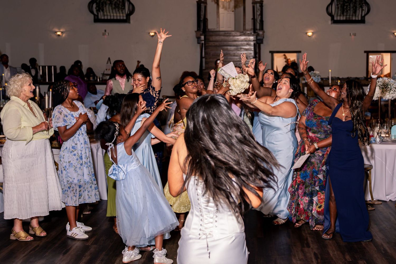 Bride tosses bouquet to excited crowd of guests during lively indoor wedding reception bouquet toss.