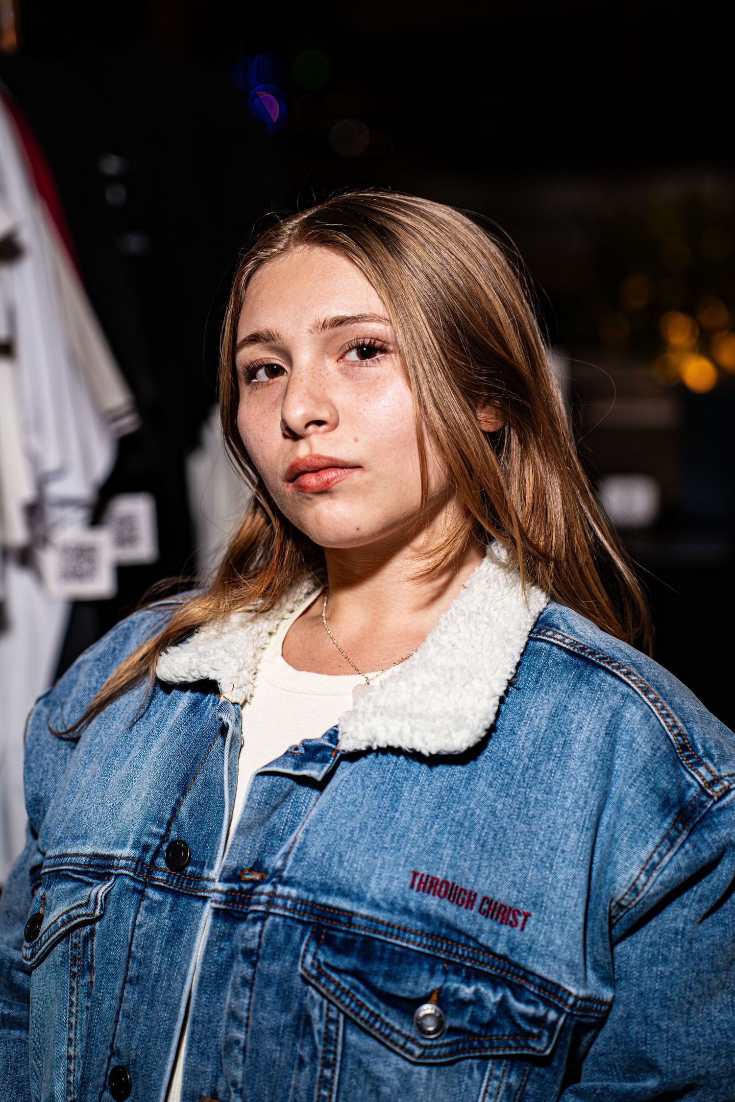 Young woman wearing Through Christ Brand denim sherpa jacket at outdoor night event.