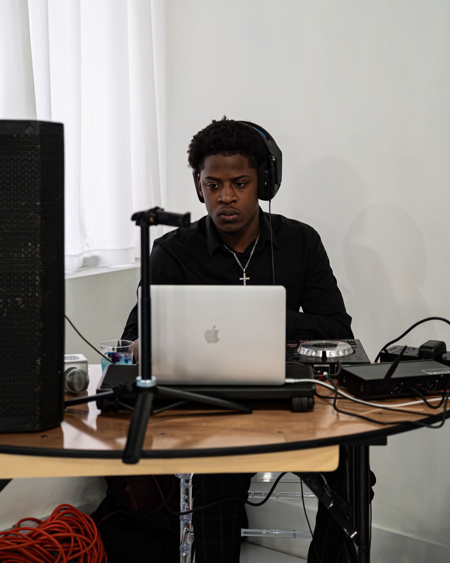 Young man wearing headphones works on MacBook at DJ and podcast setup.