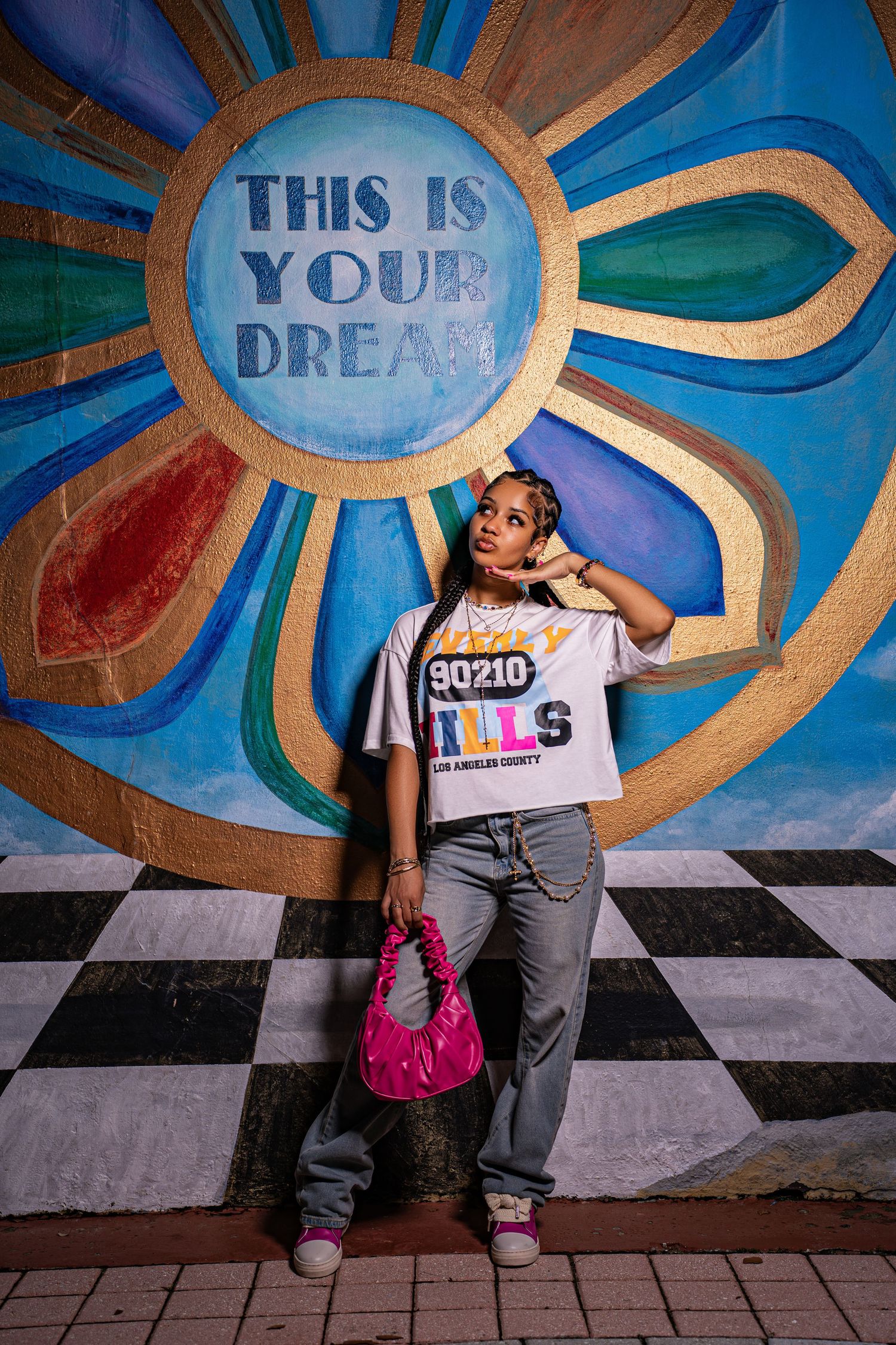 Young woman posing in front of colorful mural reading This Is Your Dream wearing 90210 Hills graphic tee and jeans.