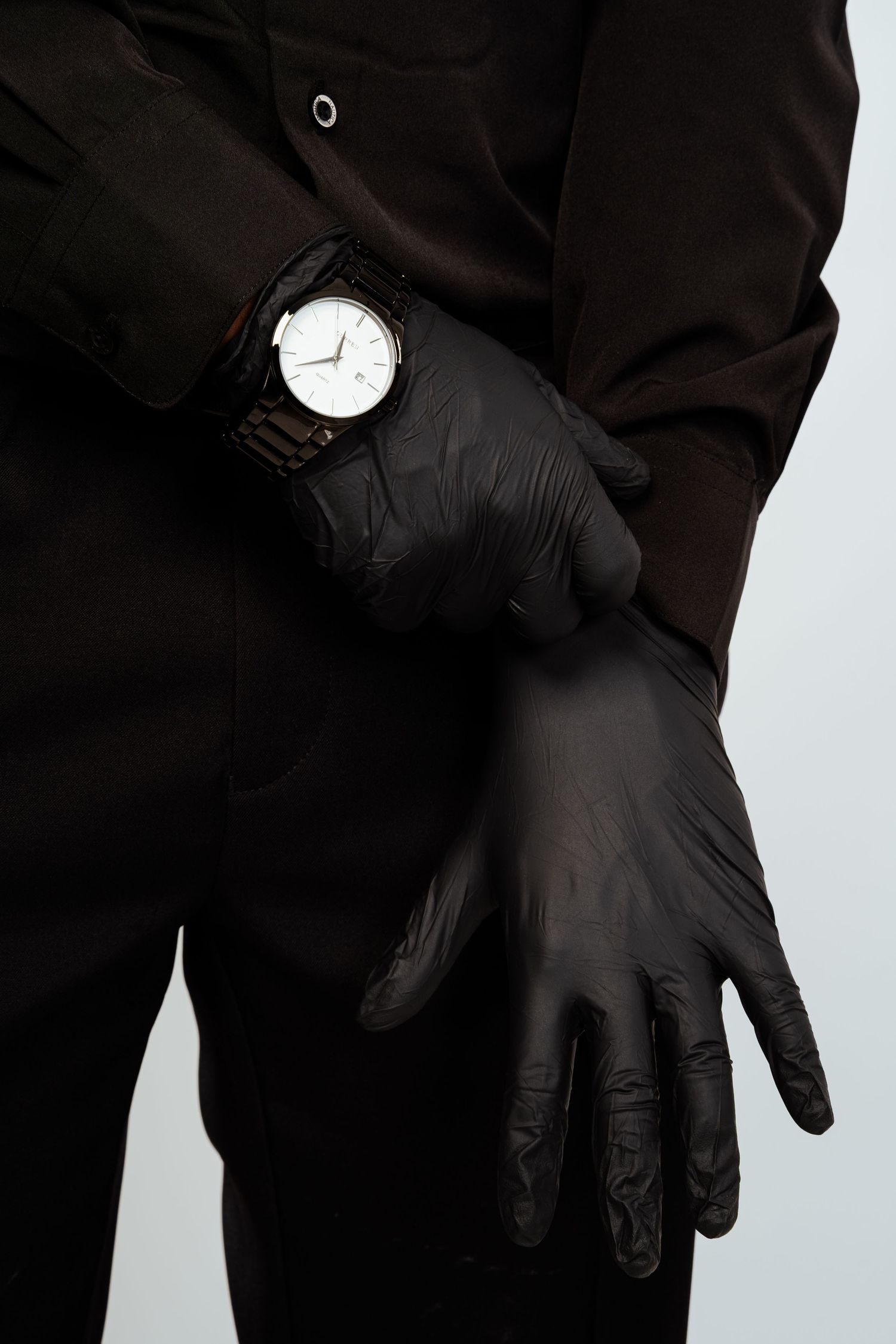Close-up of hands in black gloves adjusting a classic white-faced wristwatch.