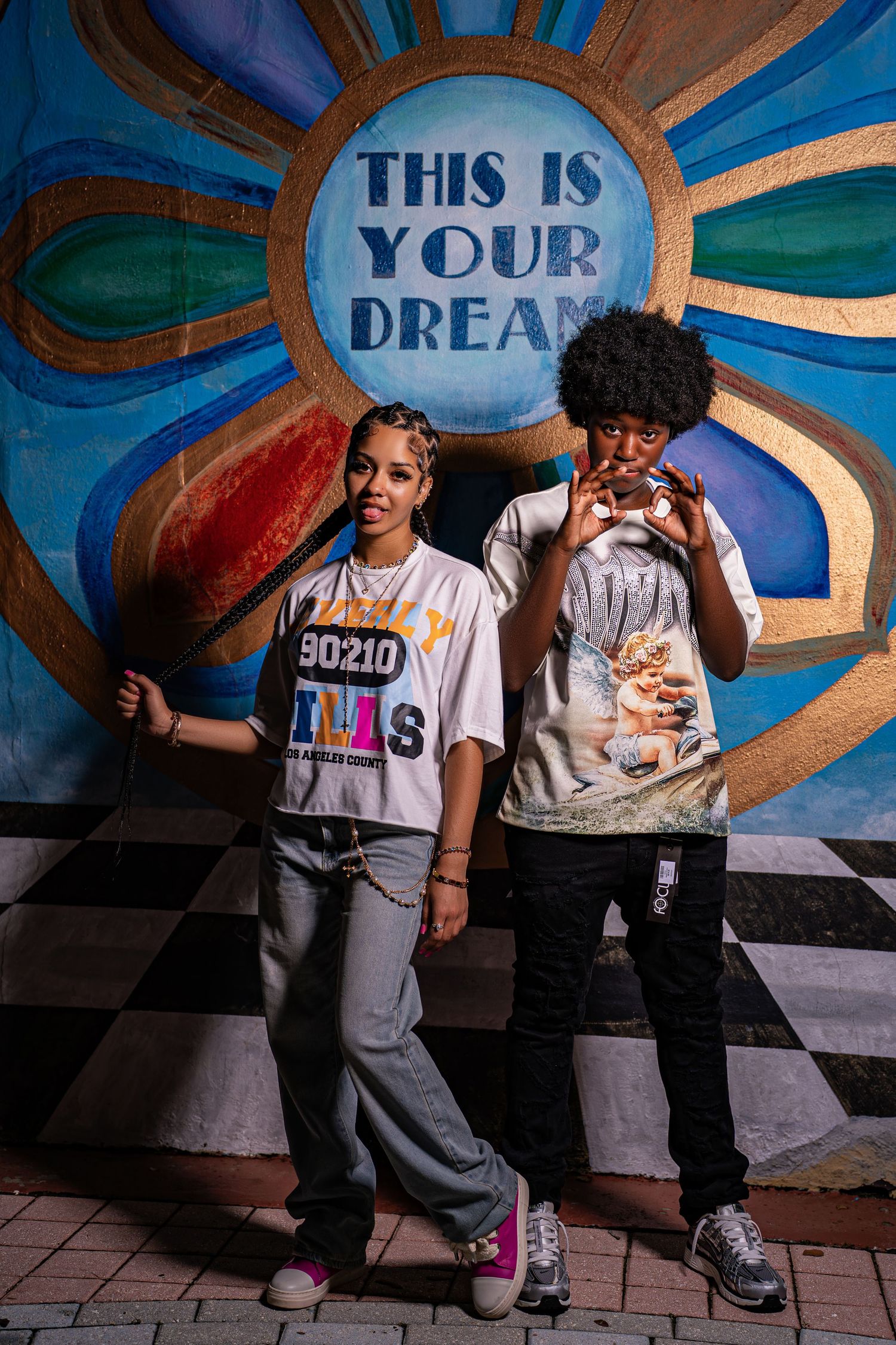 Two young people in white graphic tees smiling before colorful This Is Your Dream mural.