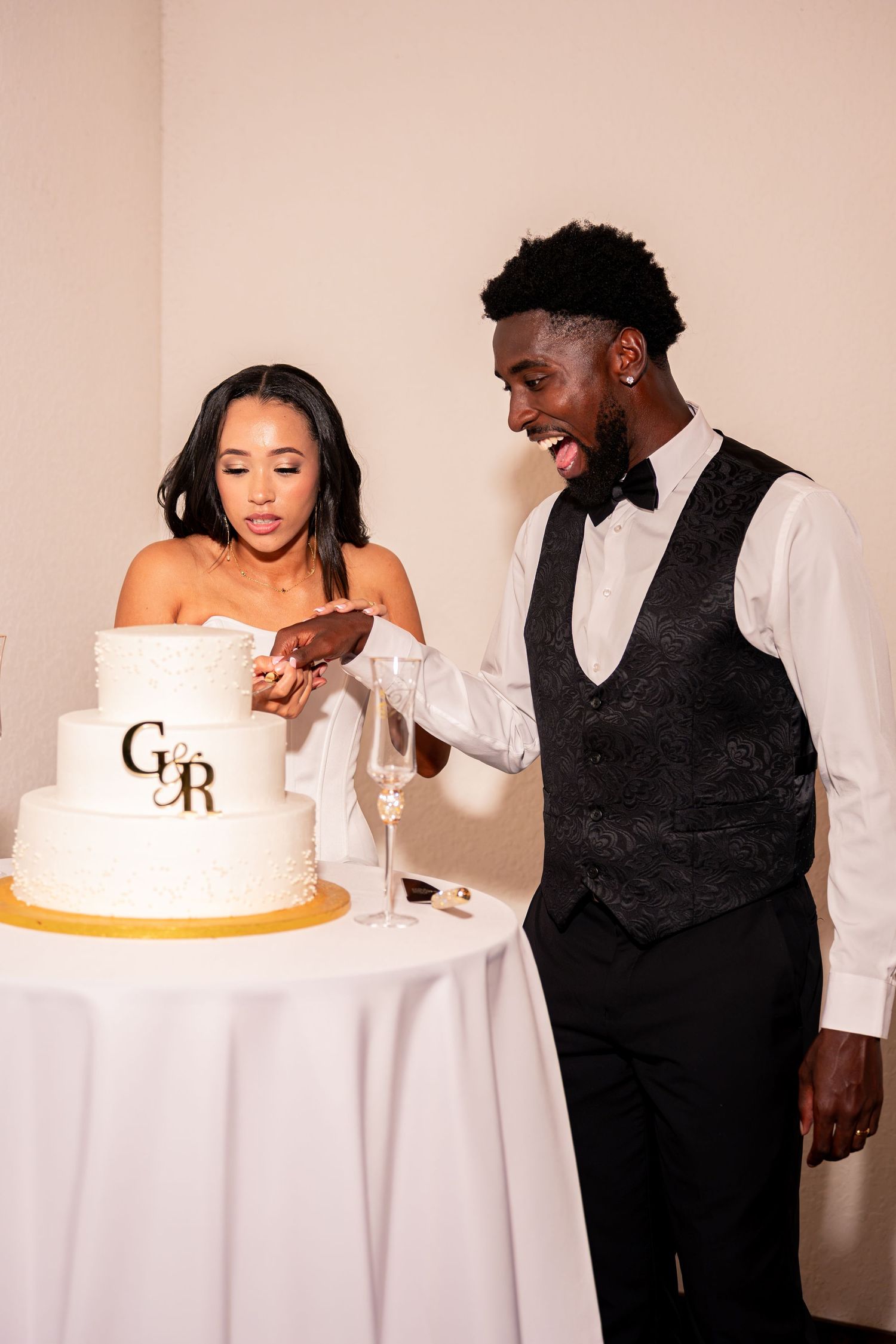 Bride and groom cut elegant two-tier white wedding cake monogrammed with G and R at their reception.