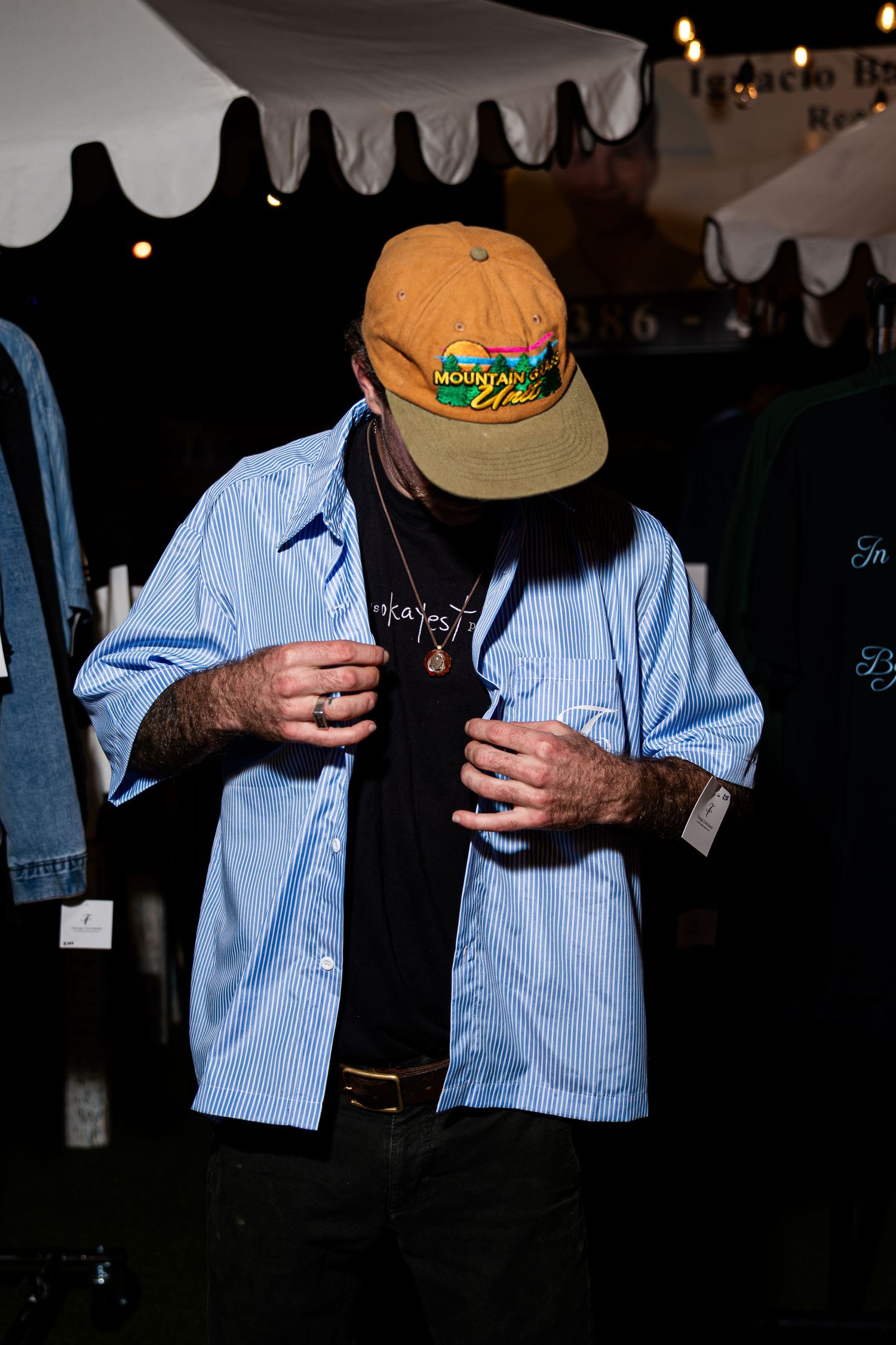 Man in orange cap and blue striped shirt looking down at clothing display at outdoor market.