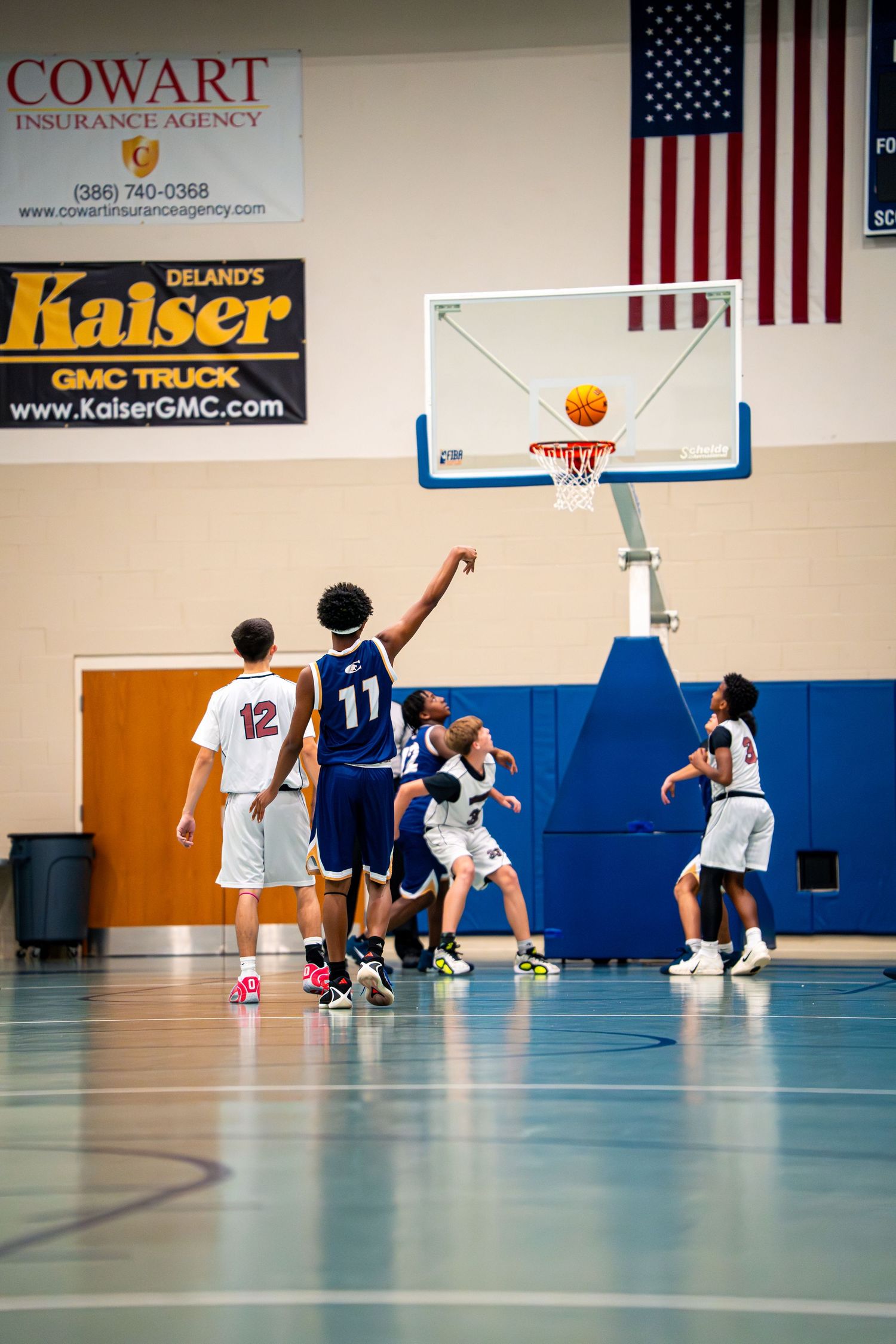 Youth basketball player #11 in blue attempts layup shot during indoor gym game with teammates.
