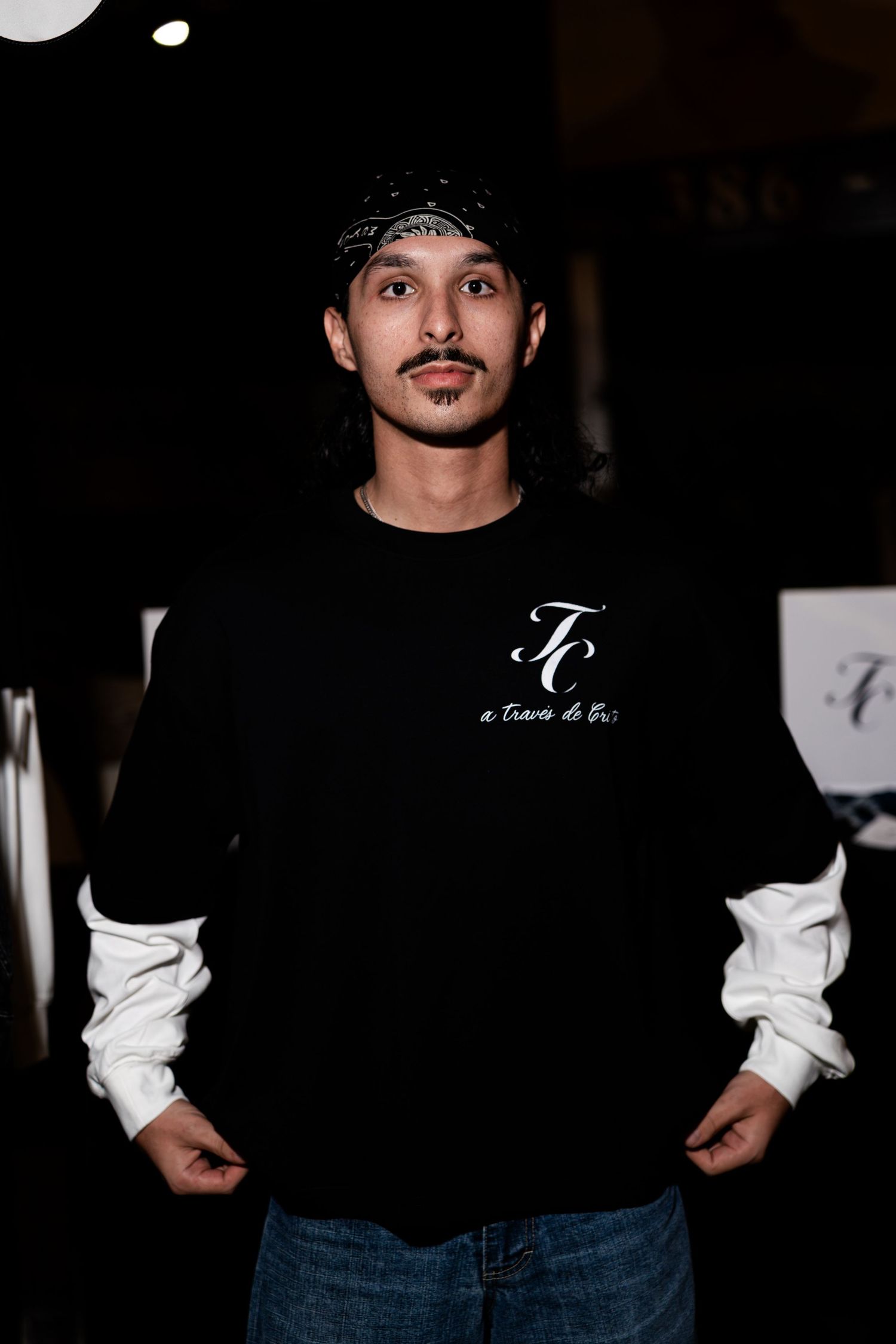 Man wearing black TC brand crewneck sweatshirt with white undershirt at outdoor night event.