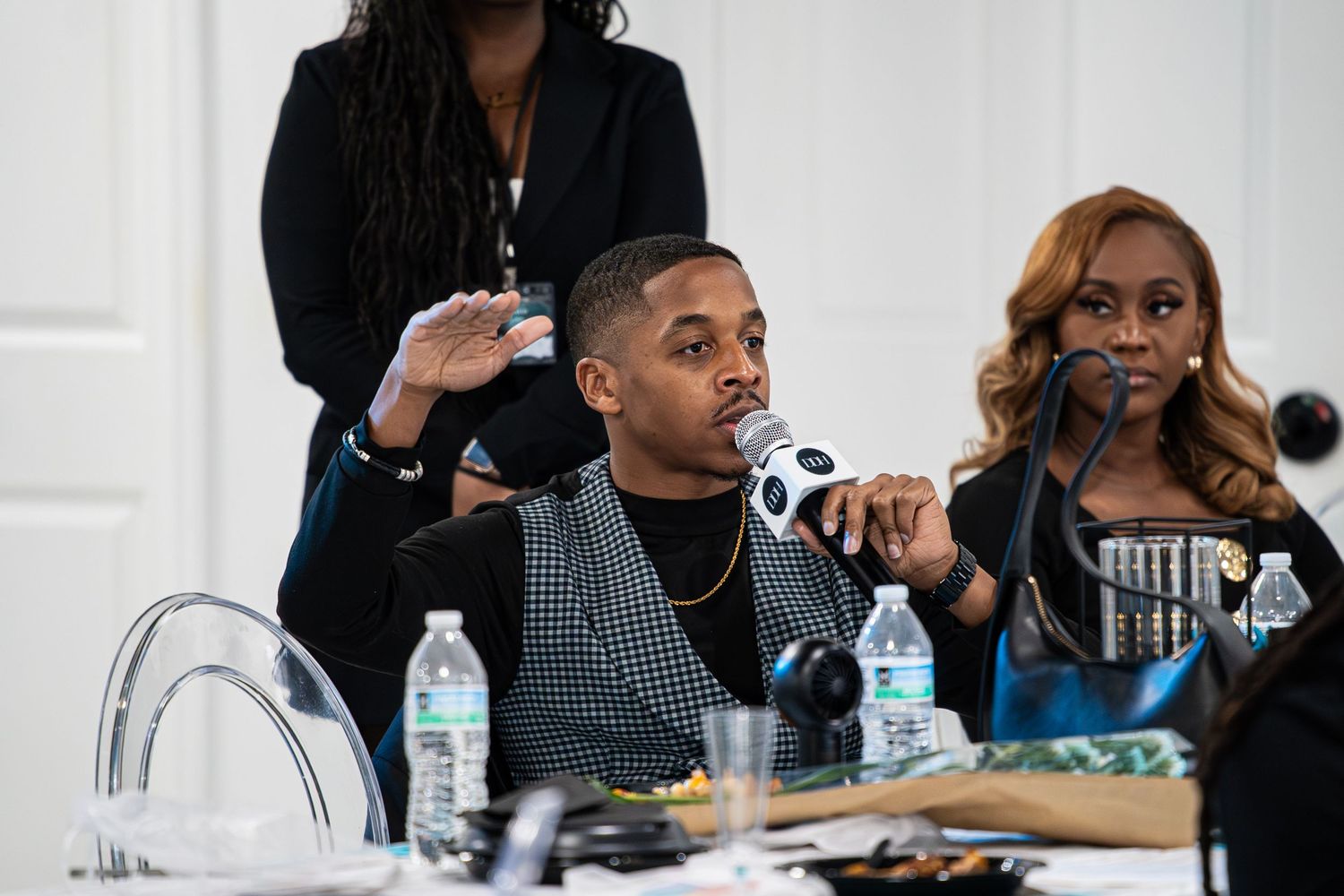 Man in checkered blazer speaks into DDH microphone at panel discussion table.