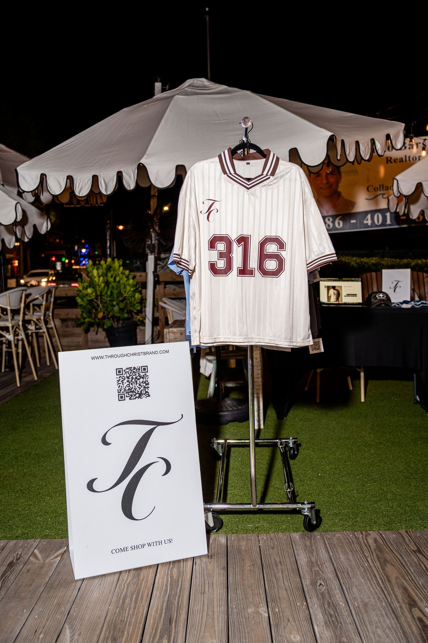 White pinstripe baseball jersey with number 316 displayed on a rack beside a TC brand sign outdoors.