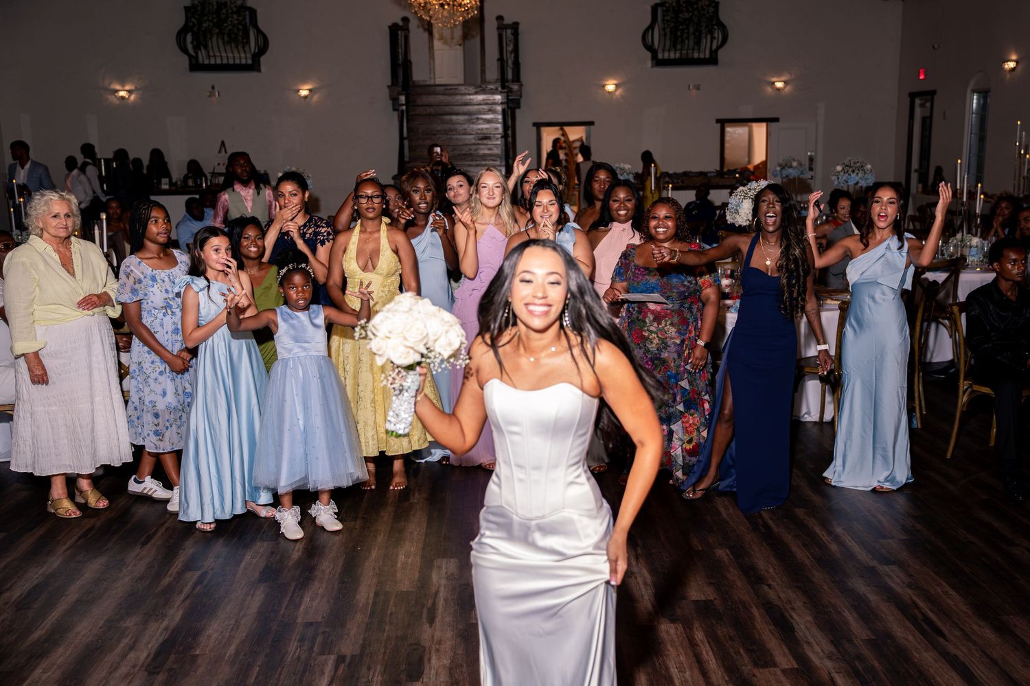 Bride prepares to toss bouquet to excited crowd of women at wedding reception.