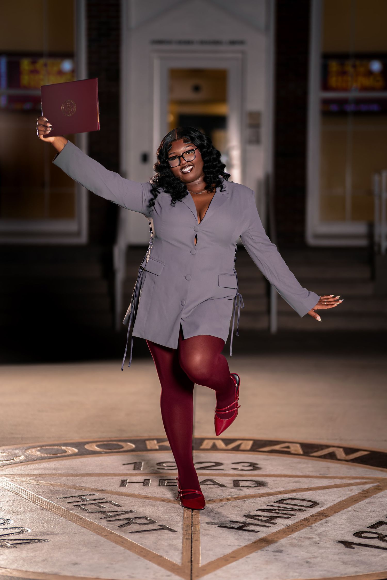A joyful Black woman celebrates graduation holding a diploma while posing on Bethune-Cookman University seal.