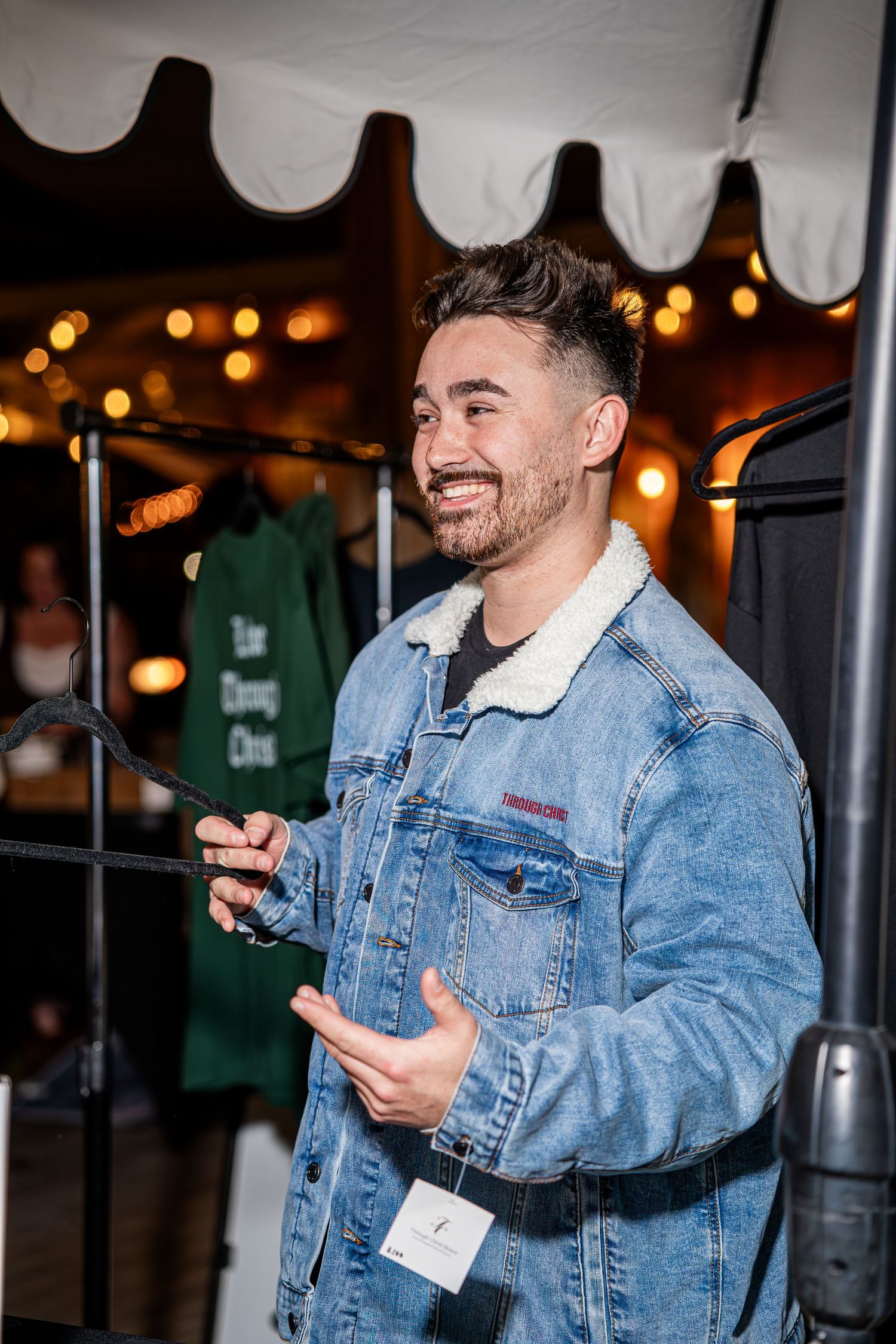 Smiling man in denim sherpa jacket with Through Christ embroidery at outdoor night event.