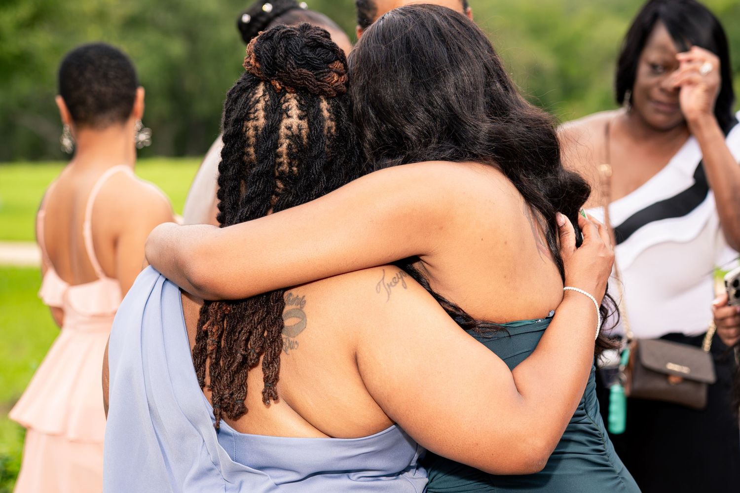 Two women share an emotional hug outdoors during wedding celebration ceremony.