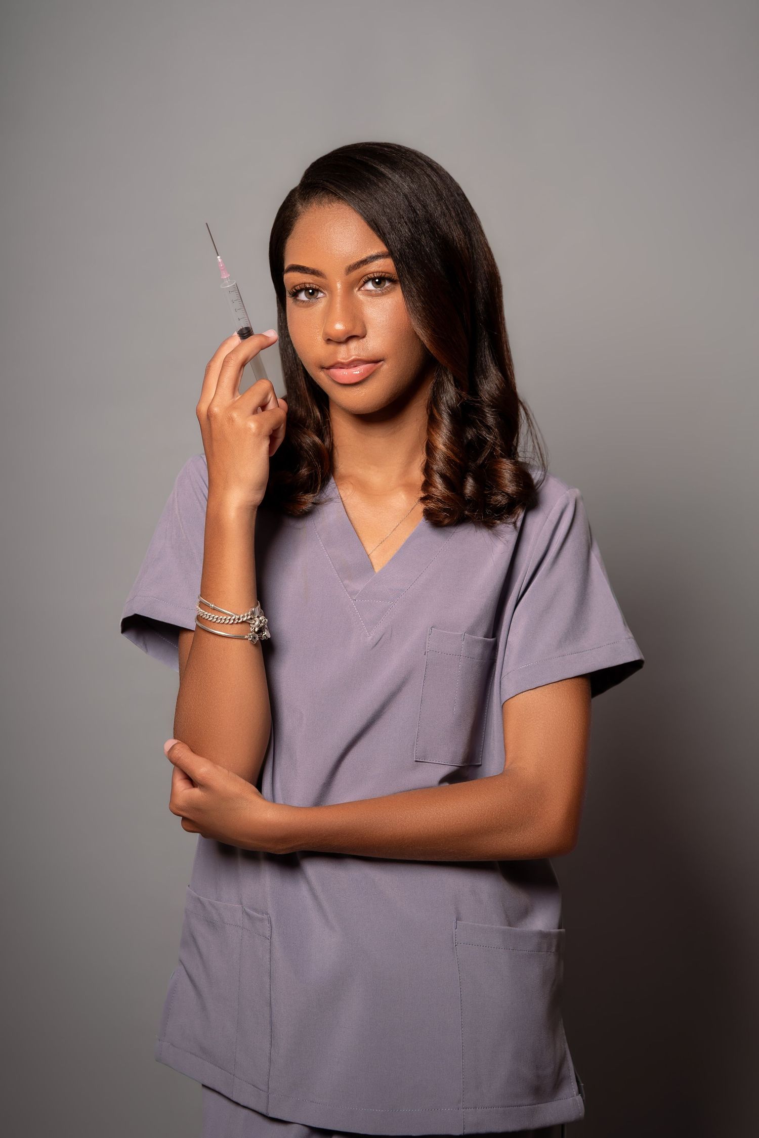 Young Black female medical professional in gray scrubs holding syringe in studio portrait.