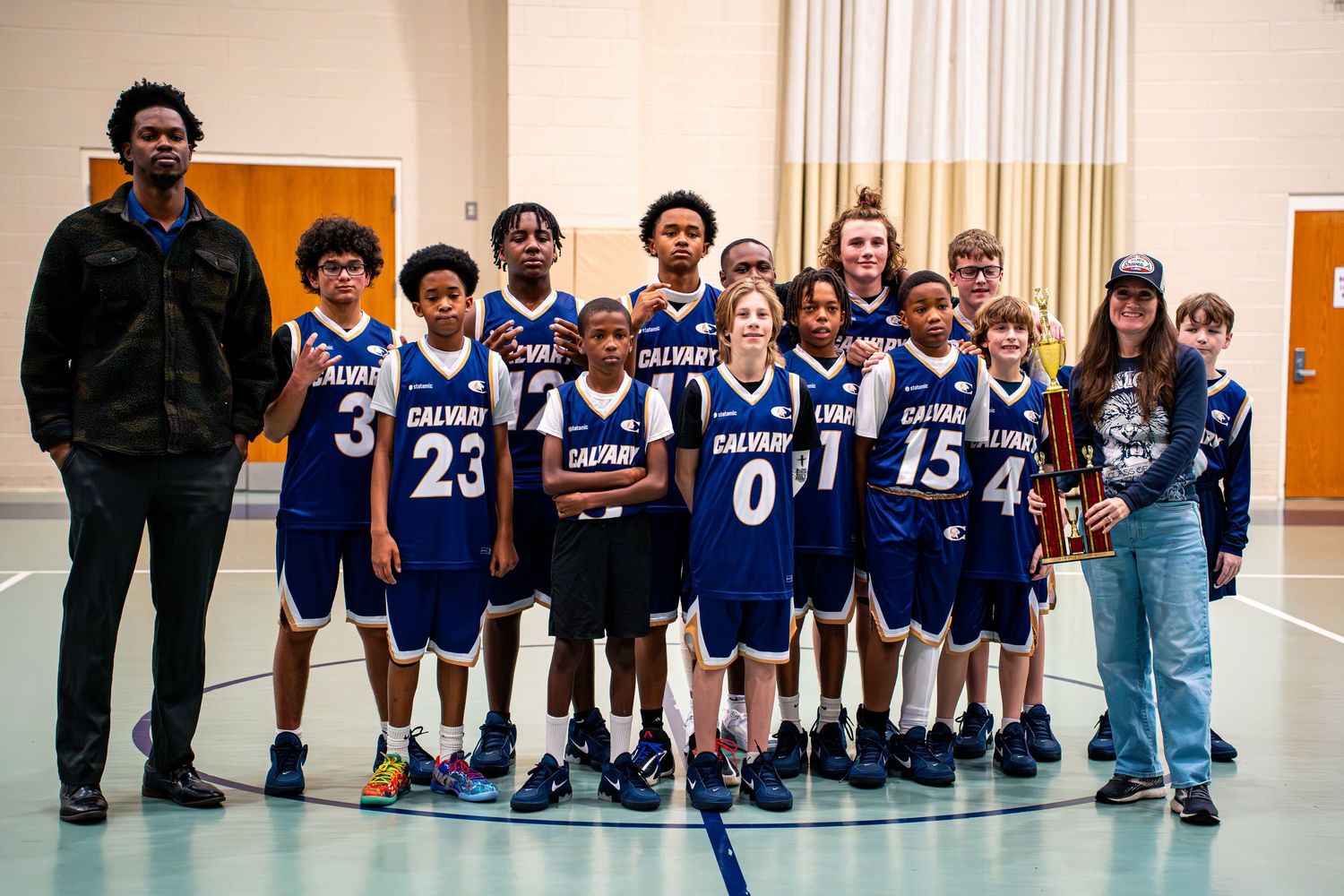 Calvary youth basketball team poses together with trophy and coaches after tournament victory indoors.