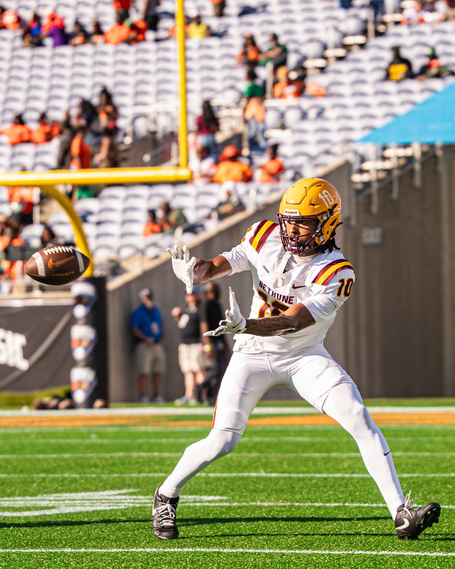 Football player in white uniform catches pass on field during college game with stadium crowd.