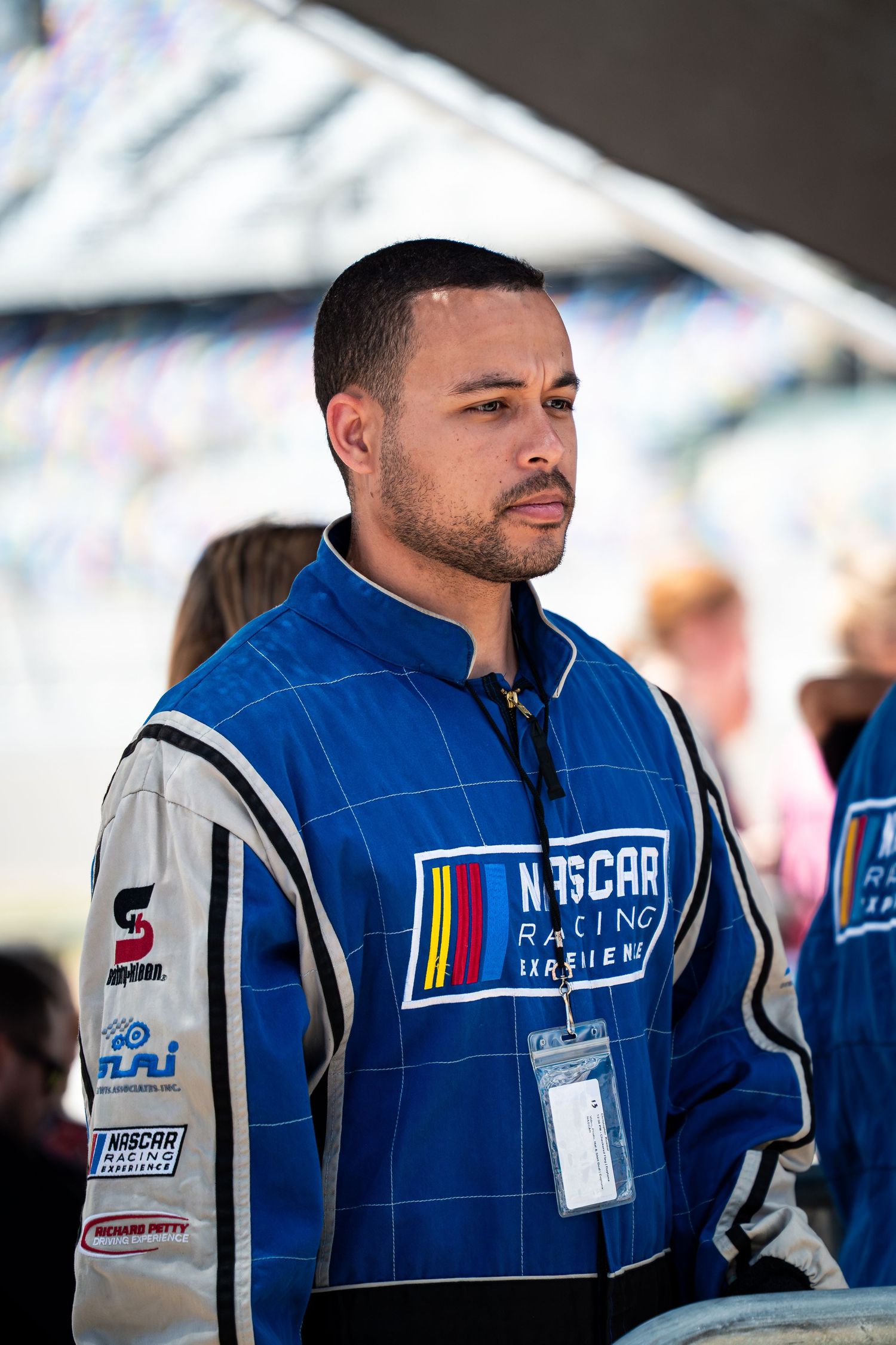 Man in blue NASCAR Racing Experience jacket standing at racing event outdoors.