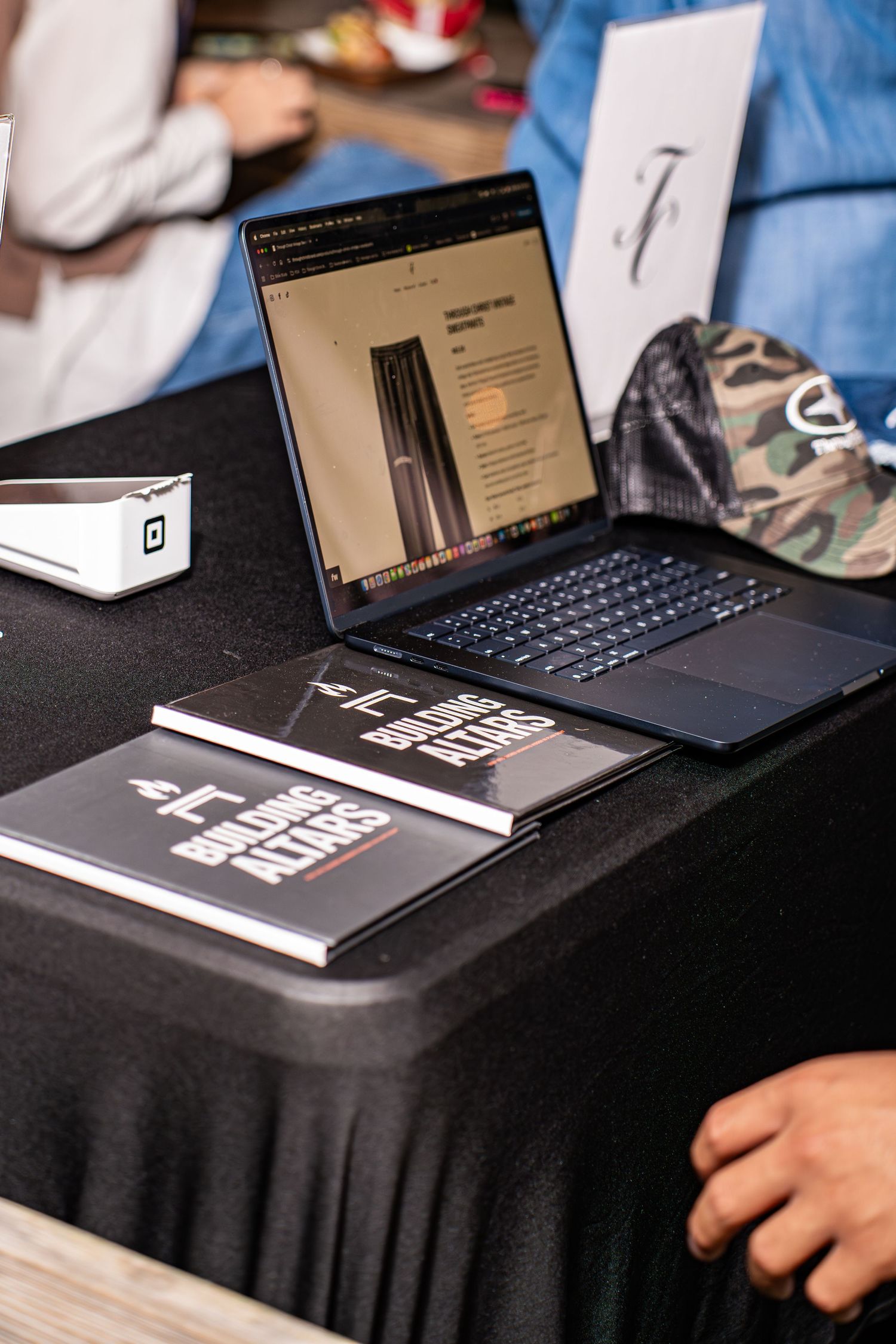 Laptop displaying TC merchandise with Building Altars books on black table at vendor booth.