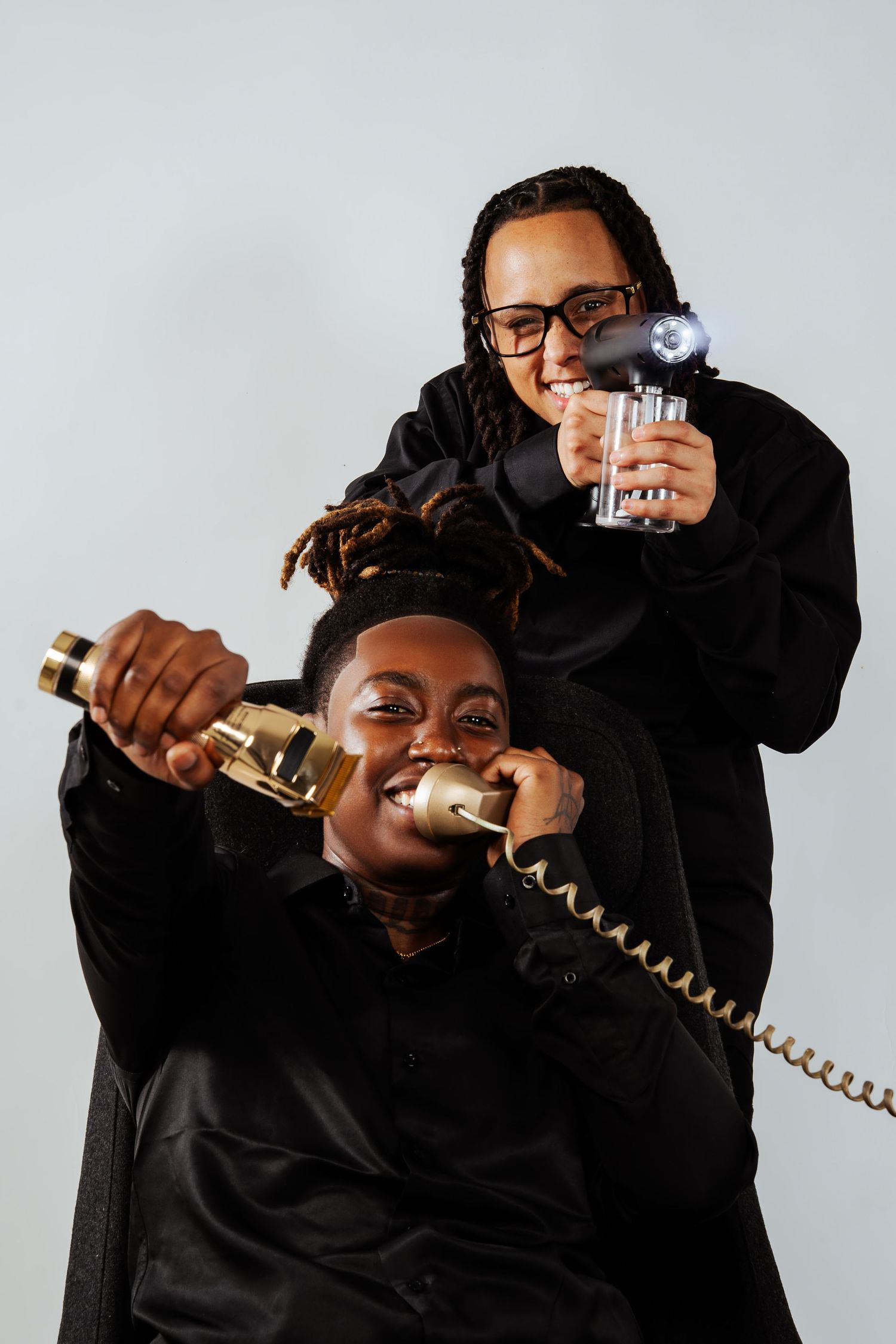 Two people in black outfits posing with gold bottle and glass cup in studio.