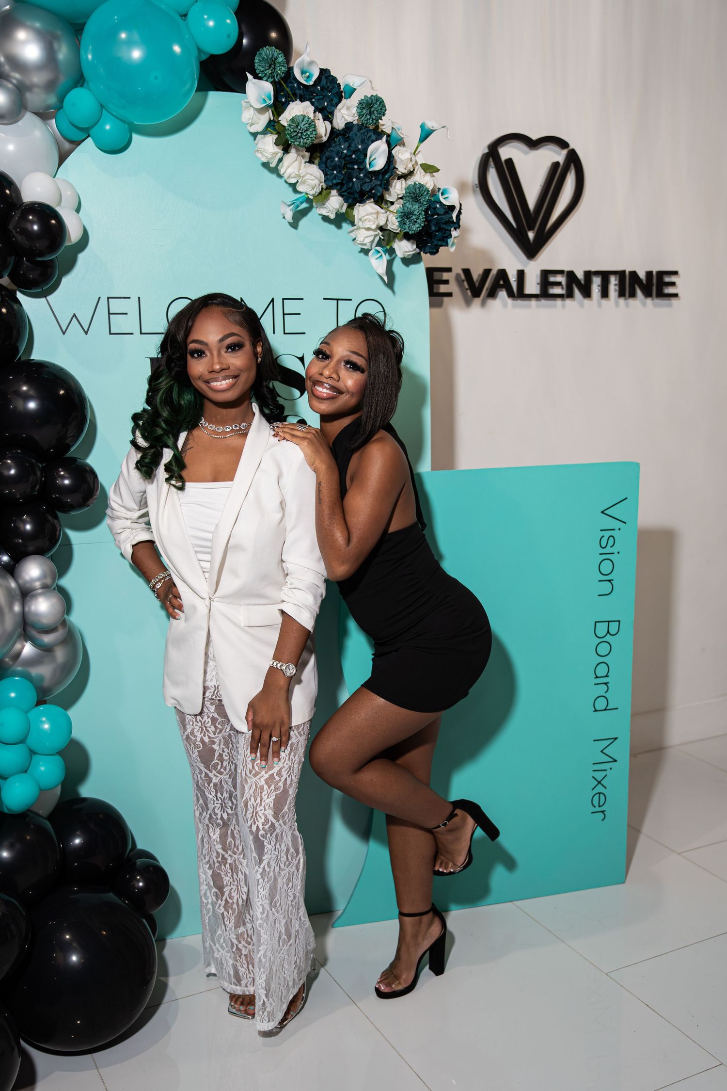 Two women pose at ESS 2026 Valentine Vision Board Mixer teal balloon backdrop.