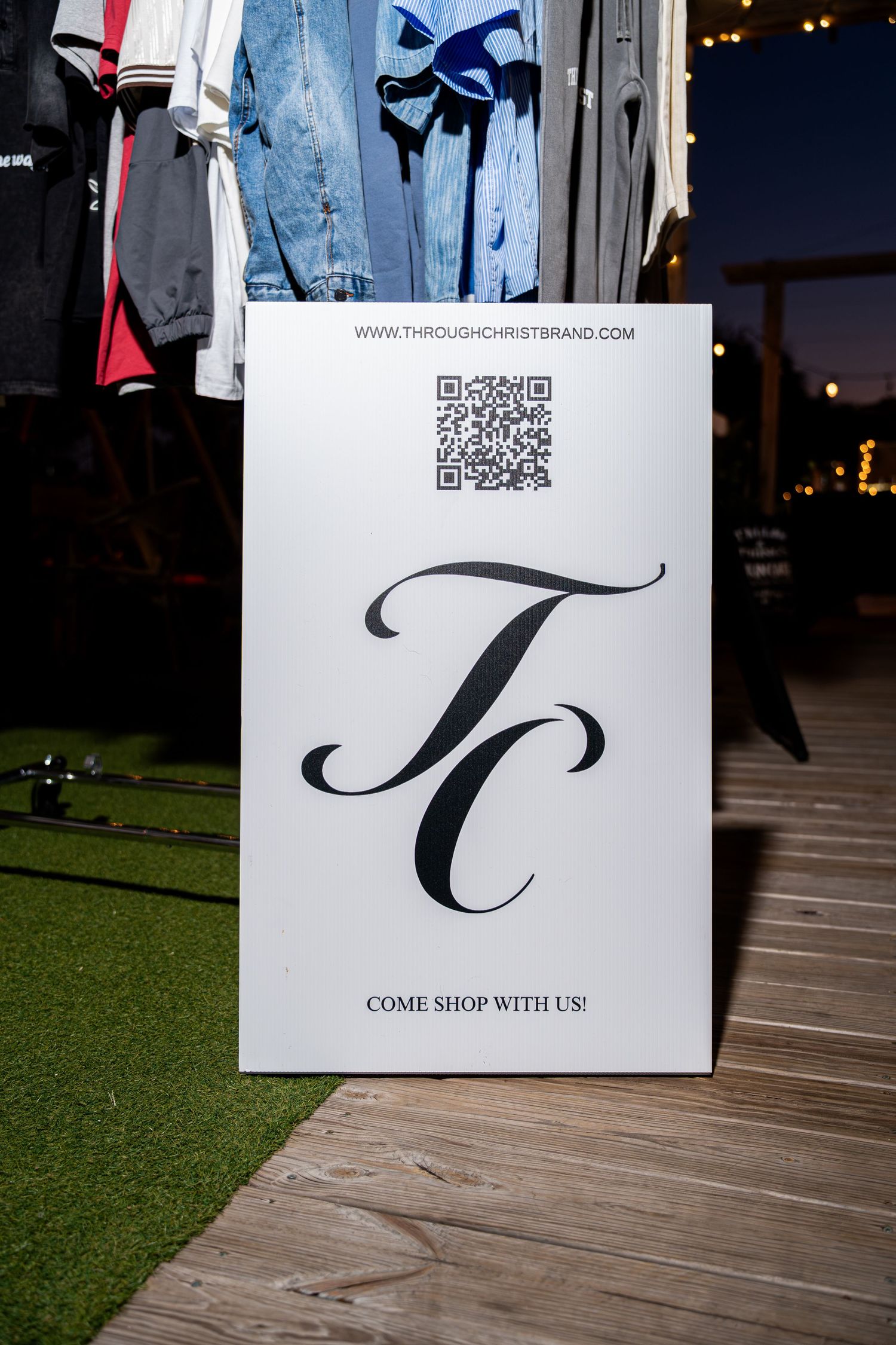 Through Christ Brand sign with TC logo and QR code displayed at an outdoor pop-up shop.