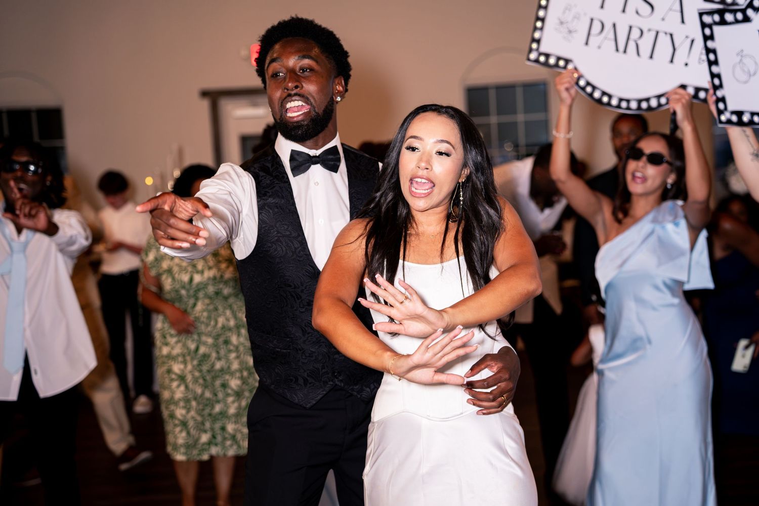 Bride and groom dance joyfully surrounded by cheering wedding guests.