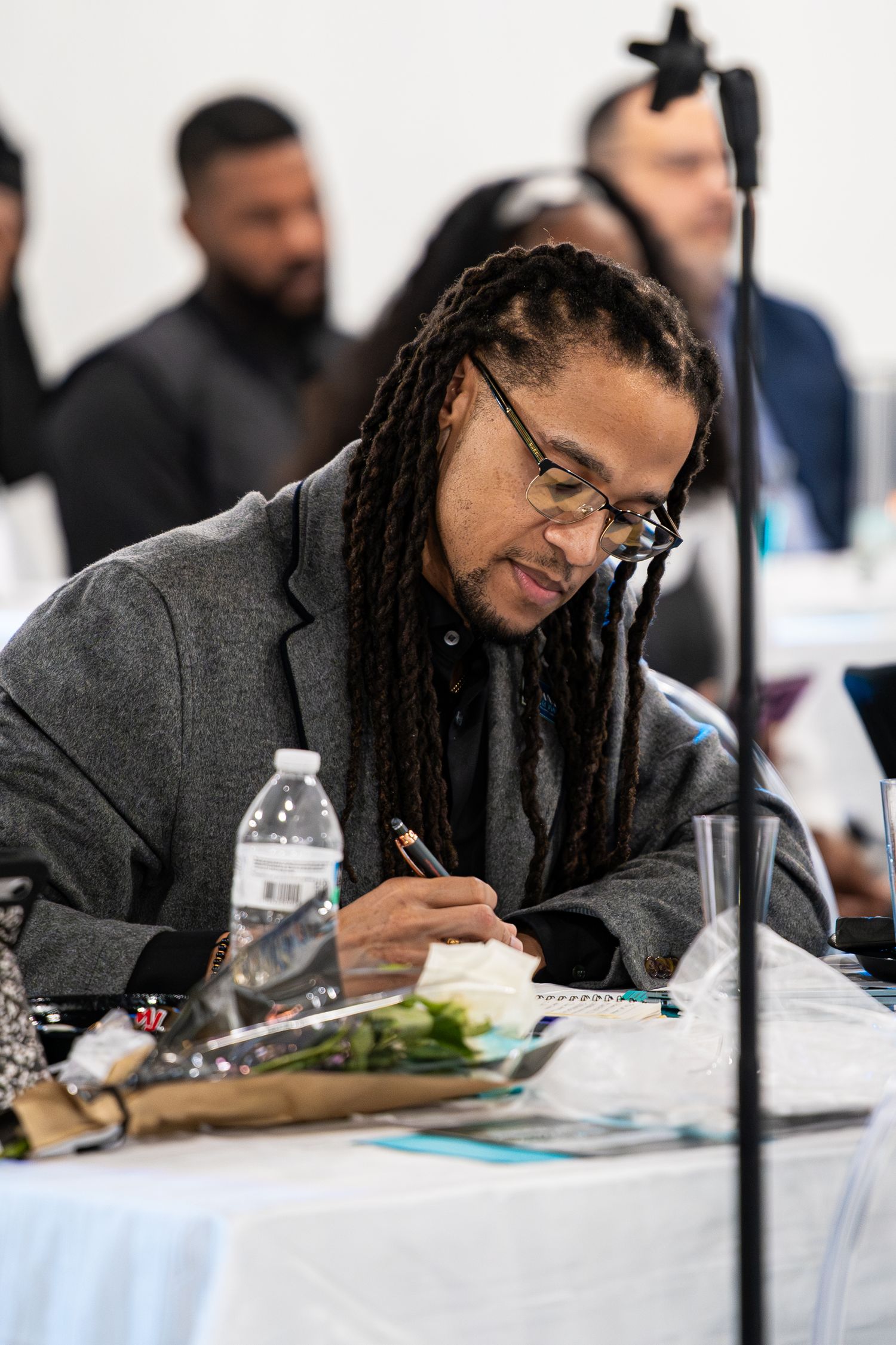 Man with long braids takes notes at professional conference or summit table.