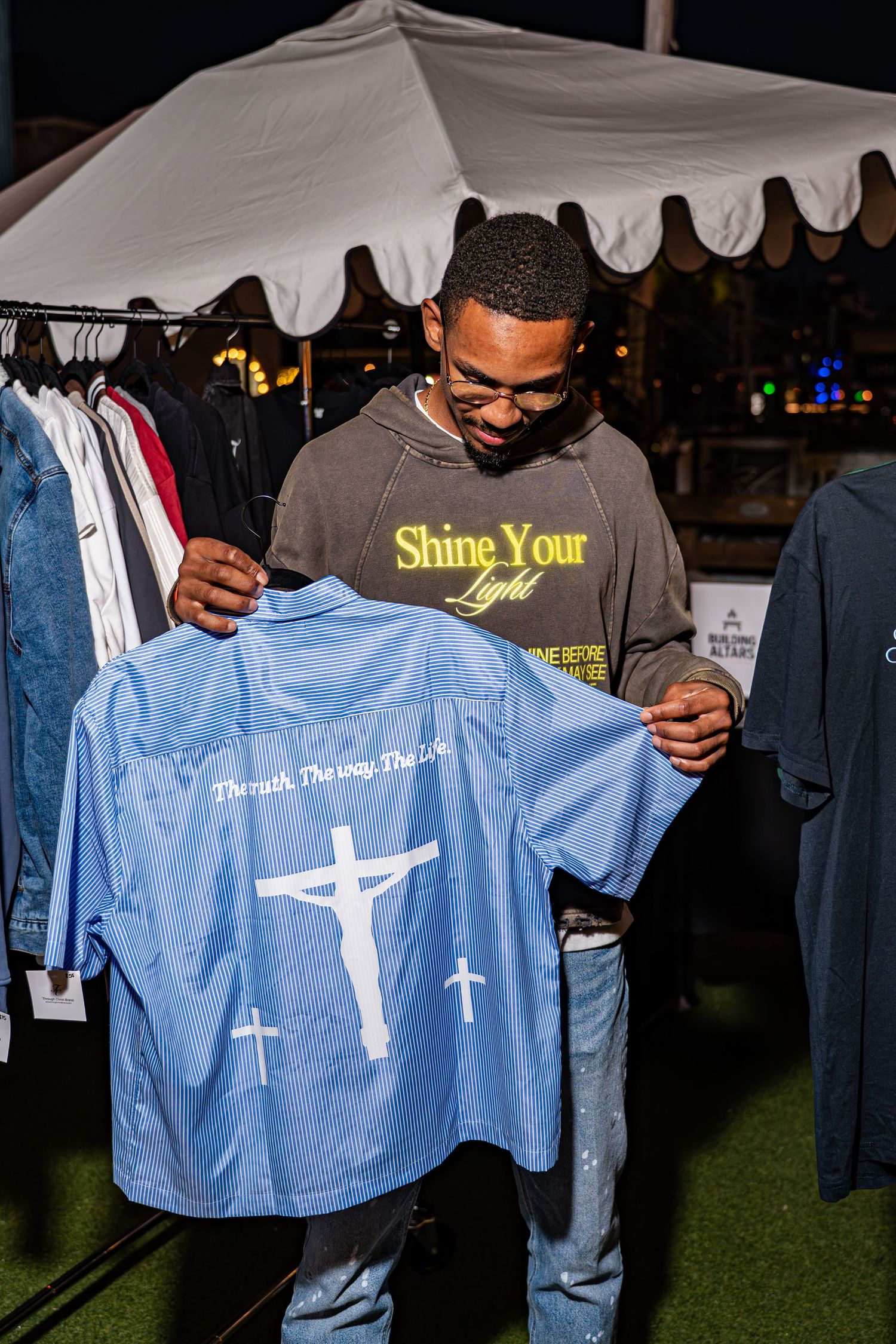 Man examining a blue Through Christ Brand shirt featuring Jesus on the cross design.
