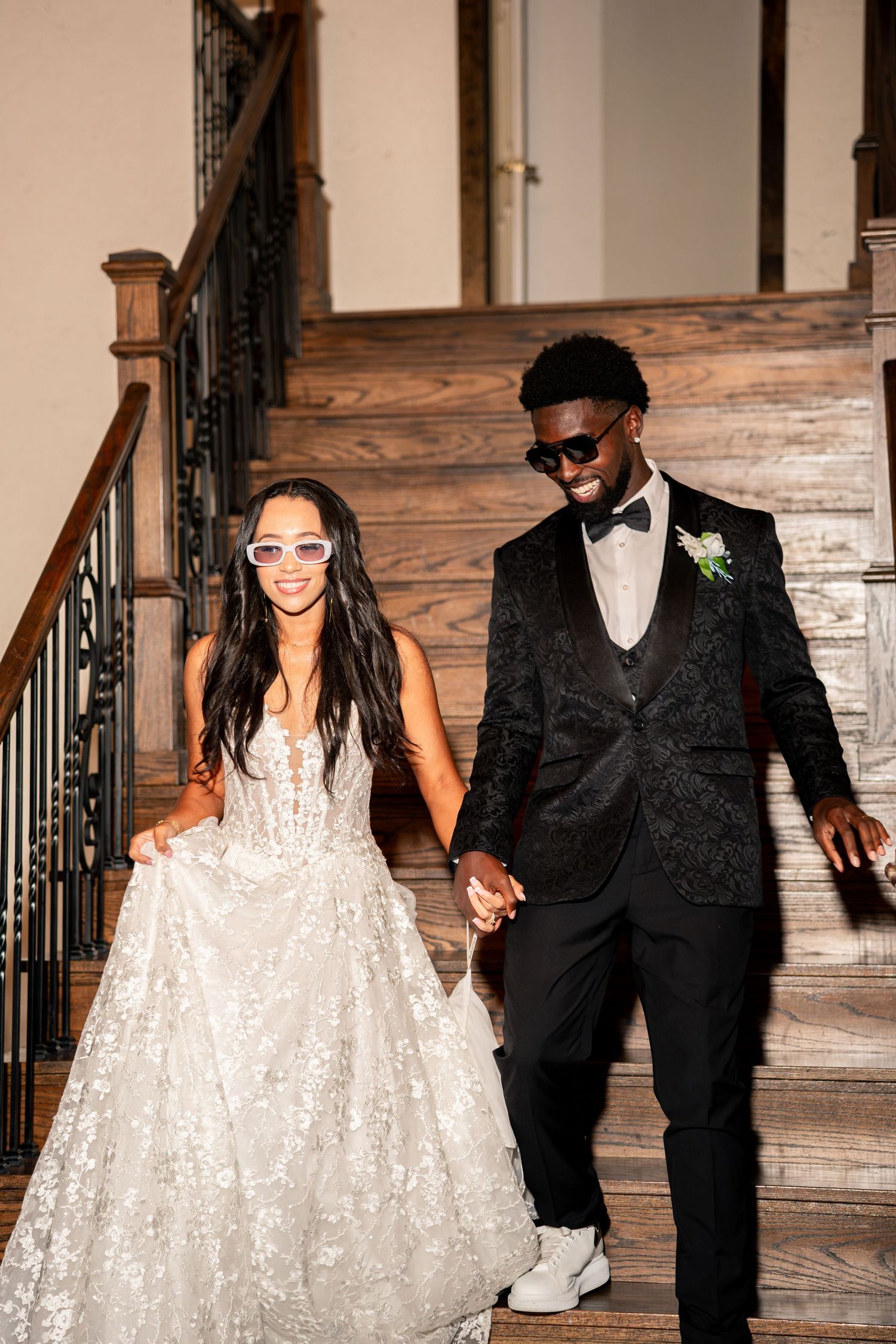 Bride and groom descend staircase wearing fun sunglasses, holding hands at wedding reception.