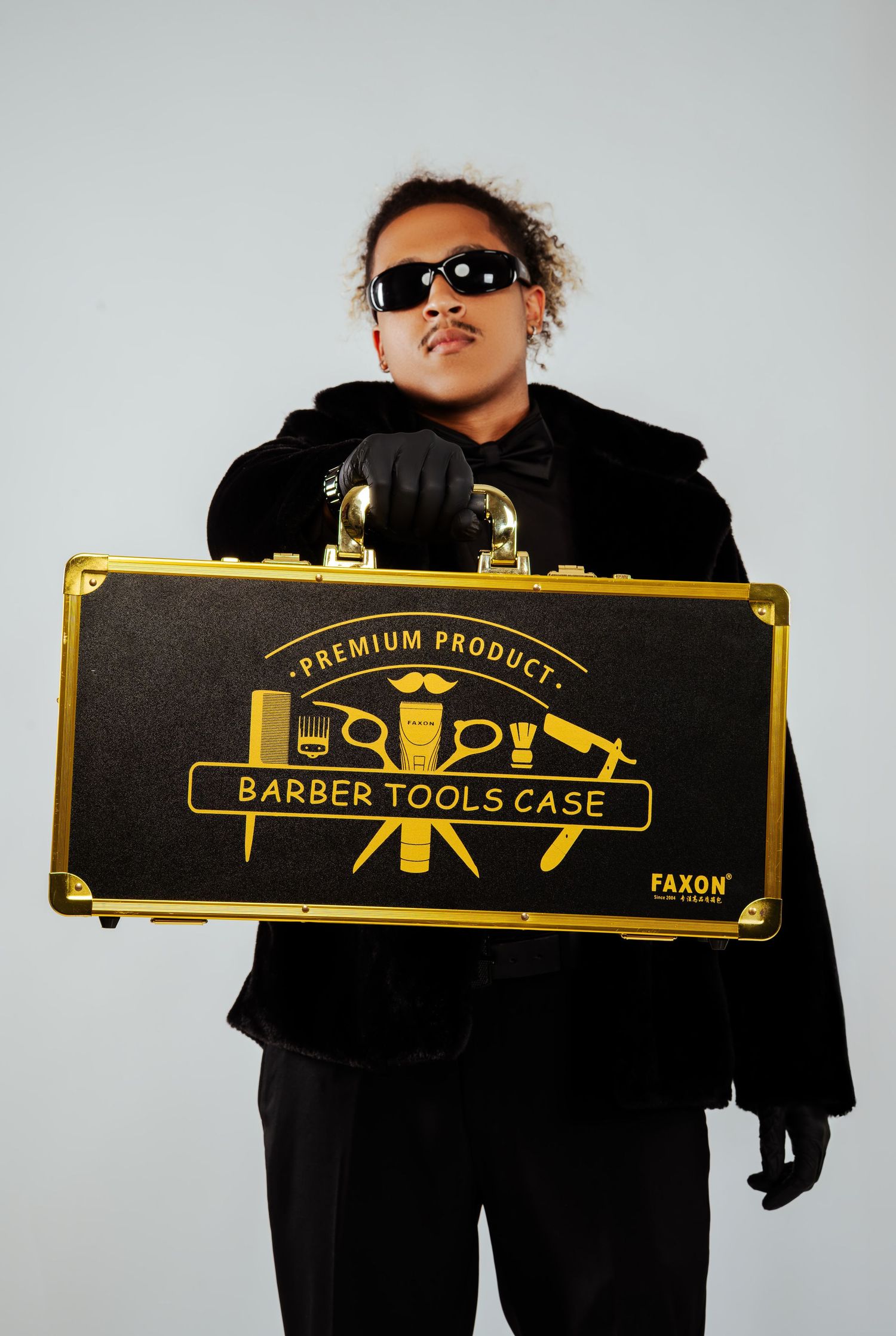 Man in black outfit holding a gold and black Faxon Barber Tools Case premium product briefcase.
