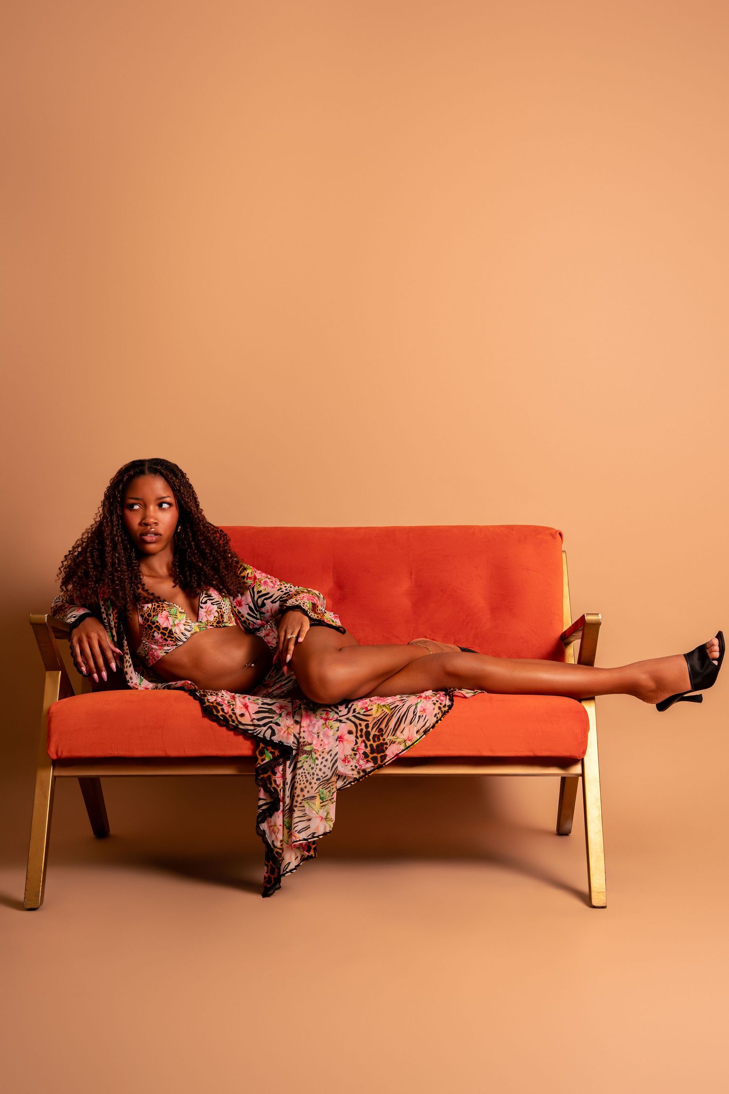 Woman in floral dress posing on orange mid-century modern sofa against beige background.