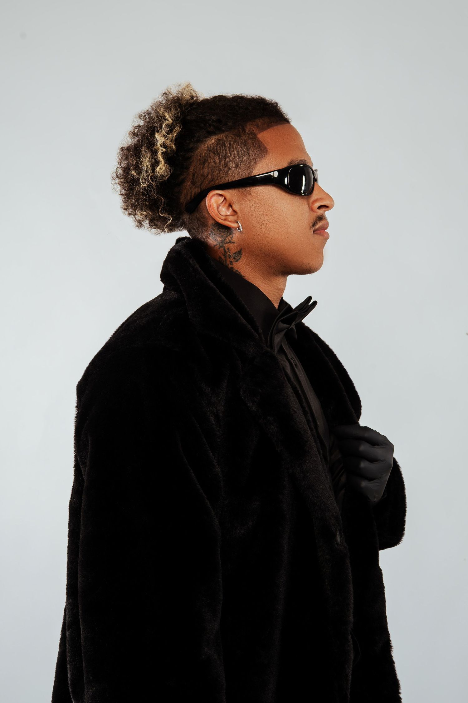 Stylish man in black fur coat and sunglasses posing in side profile view.