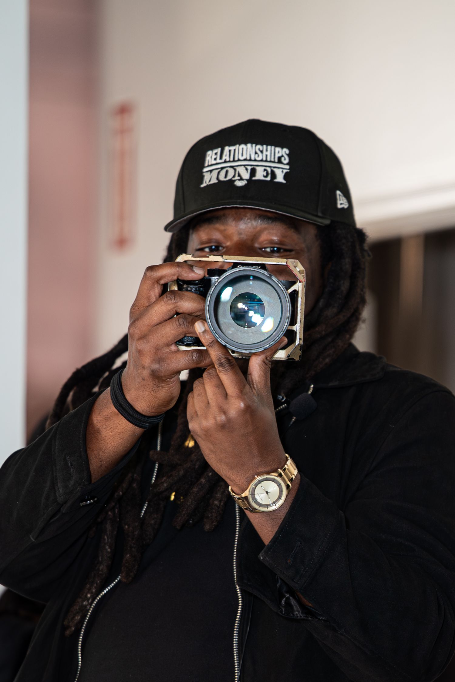 Person with dreadlocks wearing Relationships Money cap photographs with vintage camera.