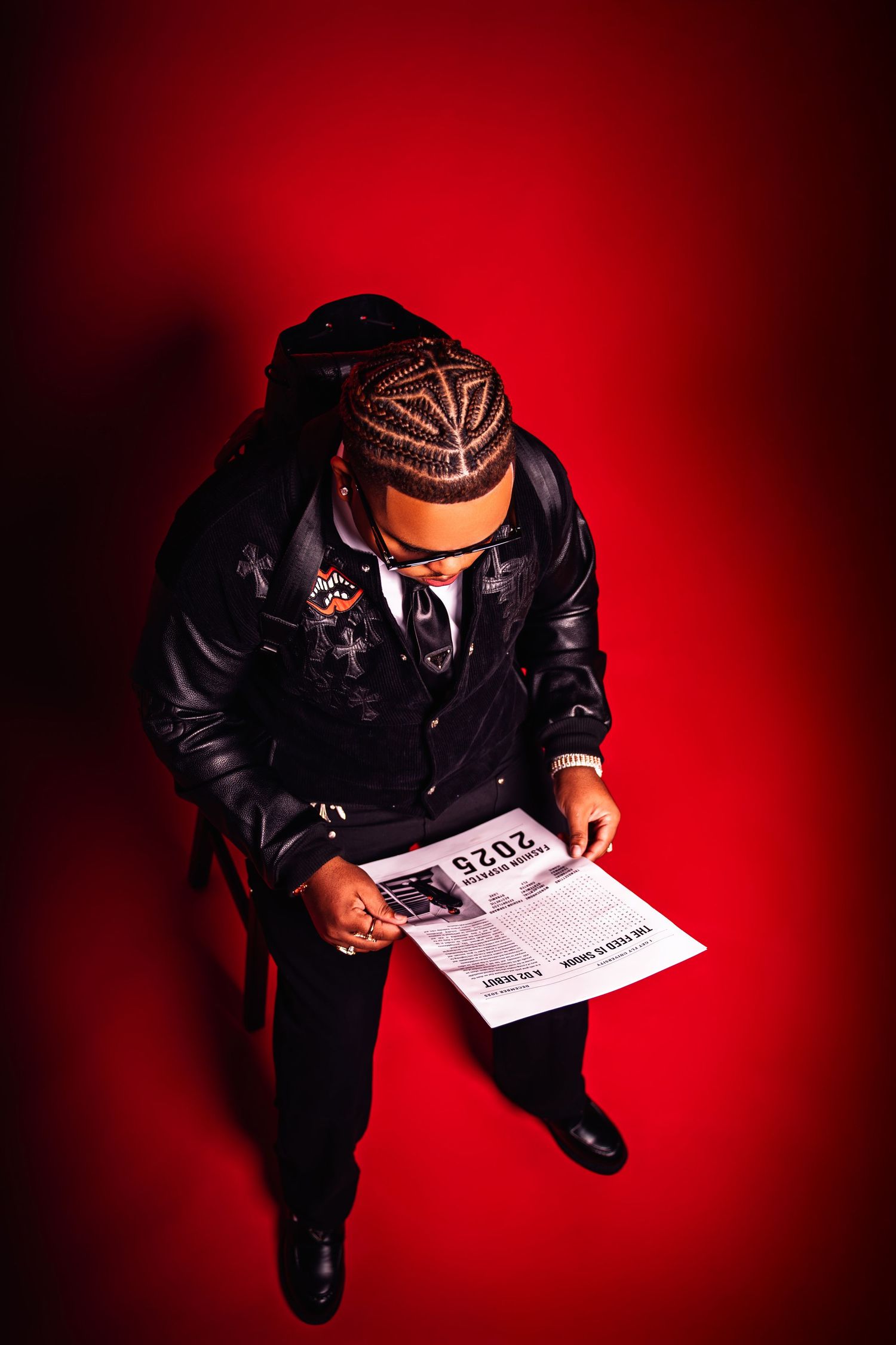 Overhead view of person in leather jacket reading newspaper on red studio background.