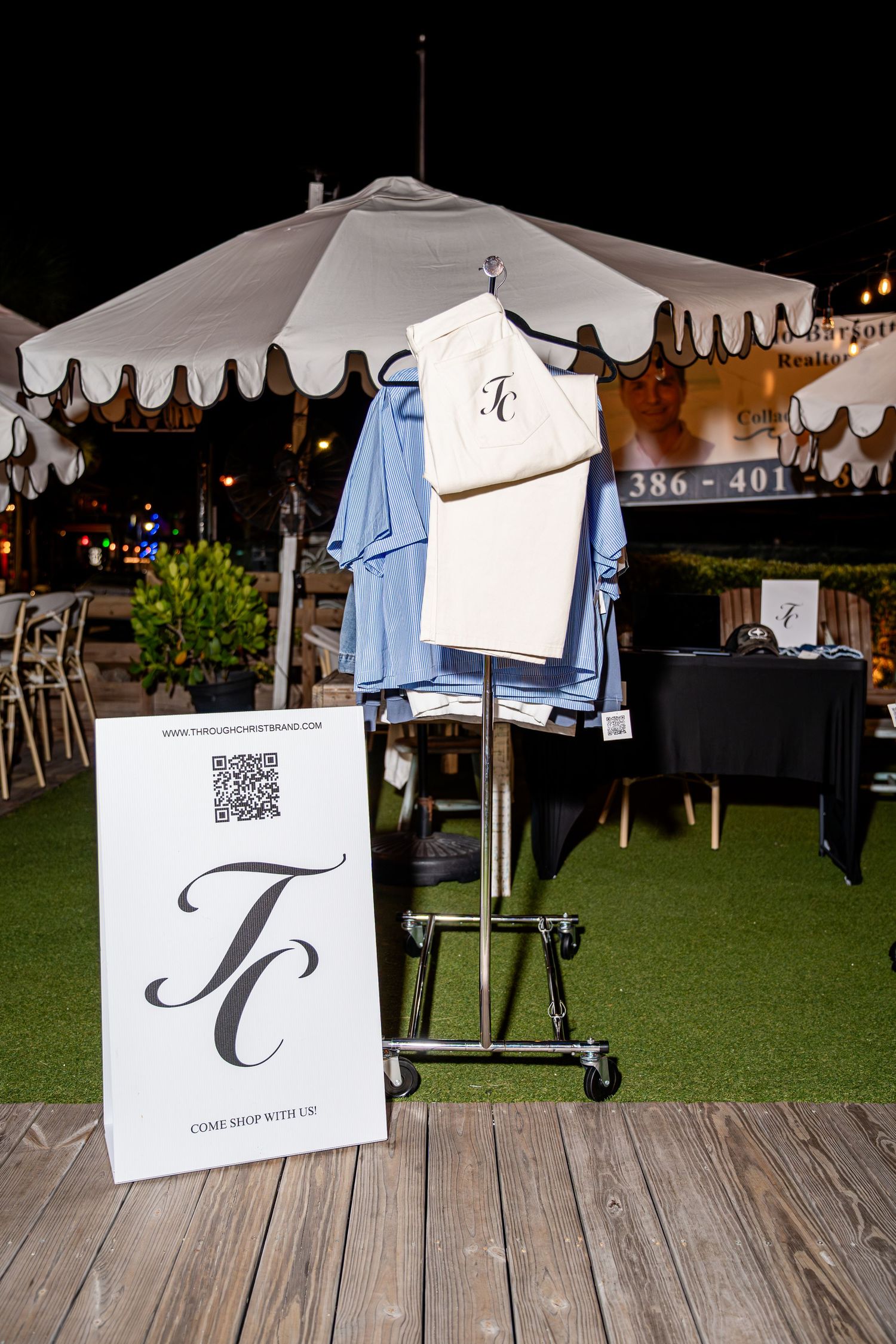 White TC monogram pants and blue shirt displayed on rack with TC brand sign at night event.